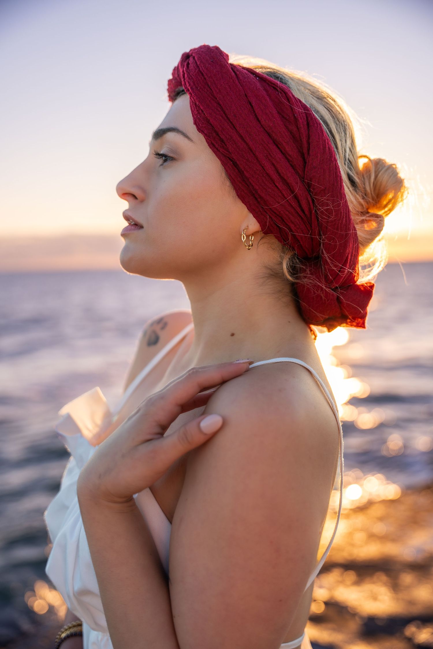 Golden hour beachside portrait in Miami – a woman with a red headscarf stands near the ocean, embracing the warm sunset glow.