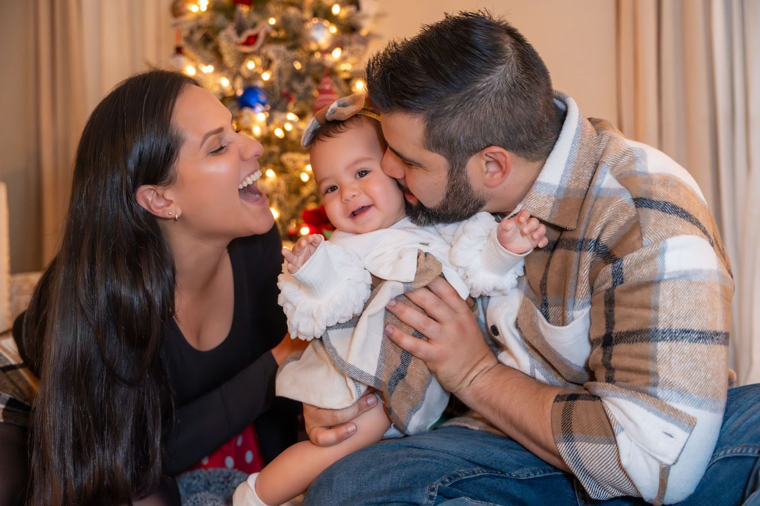 Cozy holiday family session in Pembroke Pines, FL – parents sharing a sweet moment with their baby by the Christmas tree.