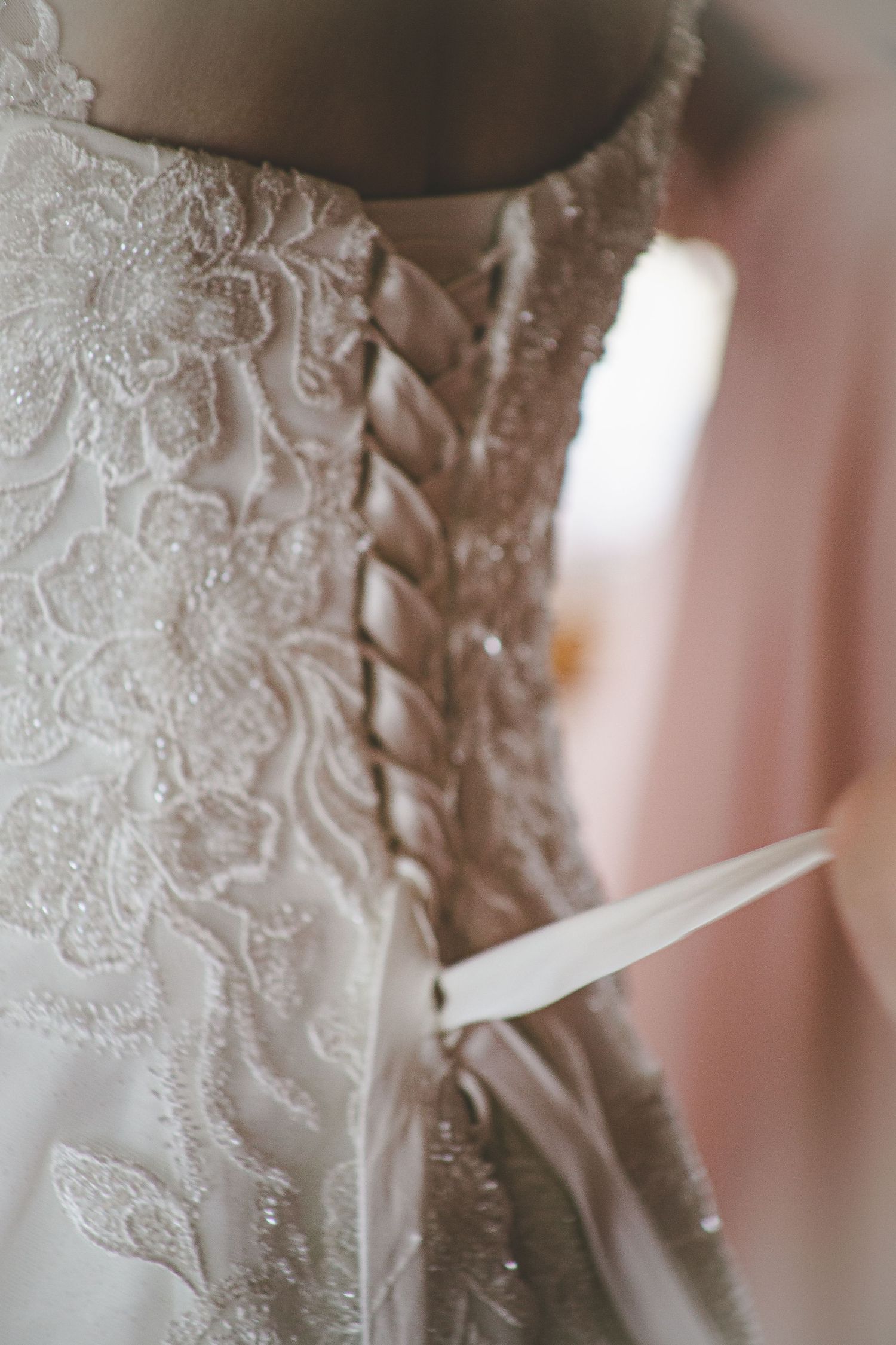 Detailed close-up of intricate lace and corset back detailing on a white wedding dress.