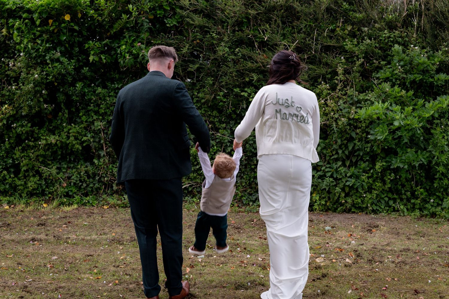A couple in formal attire walks together through a lush green garden setting during a special occasion.