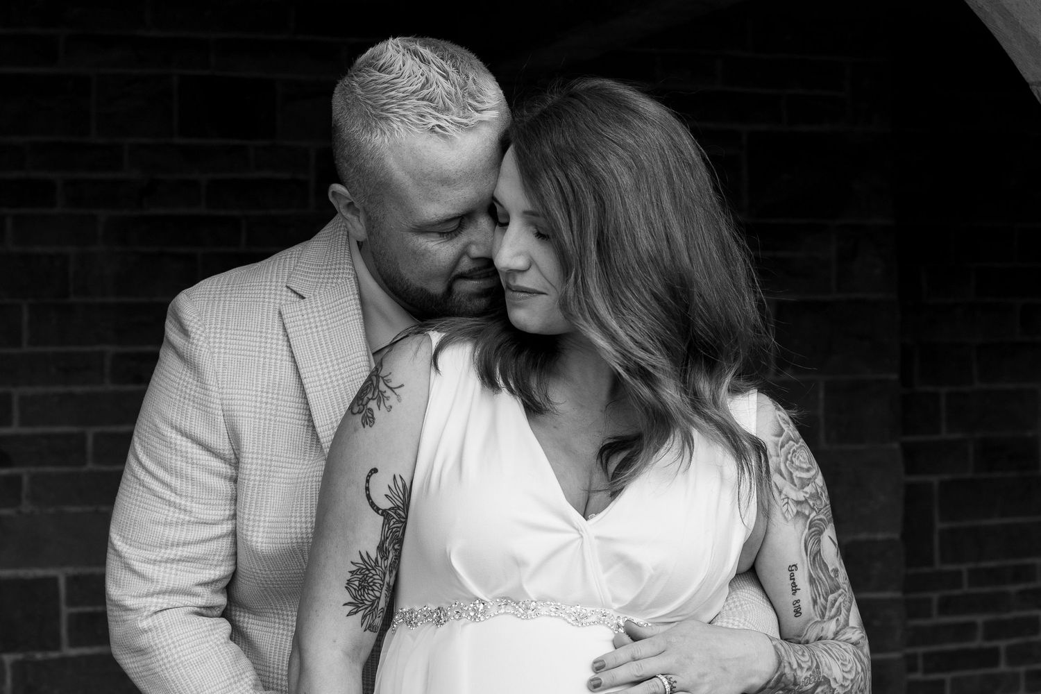 Romantic monochrome portrait of newlyweds sharing tender moment against dark background.