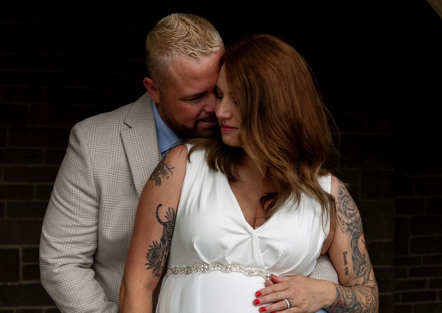 Intimate black and white wedding photo showing couple embracing in front of brick wall.
