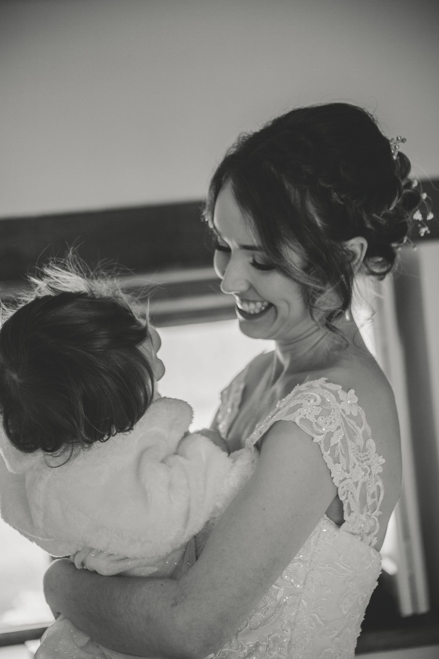 A tender black and white moment between a bride in lace and a child sharing laughter and embrace.