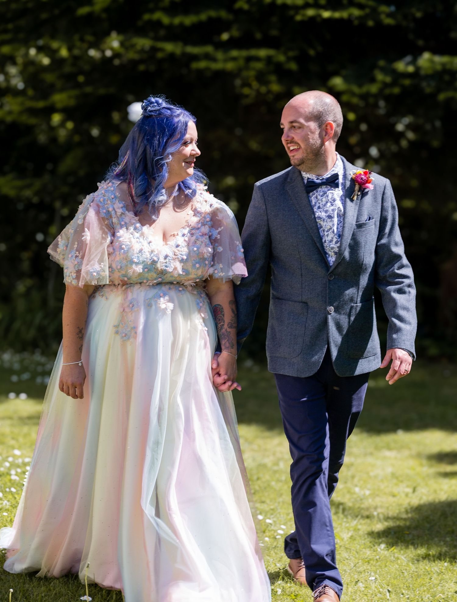 A couple shares a joyful moment walking together outdoors on their wedding day in a sunny garden setting.
