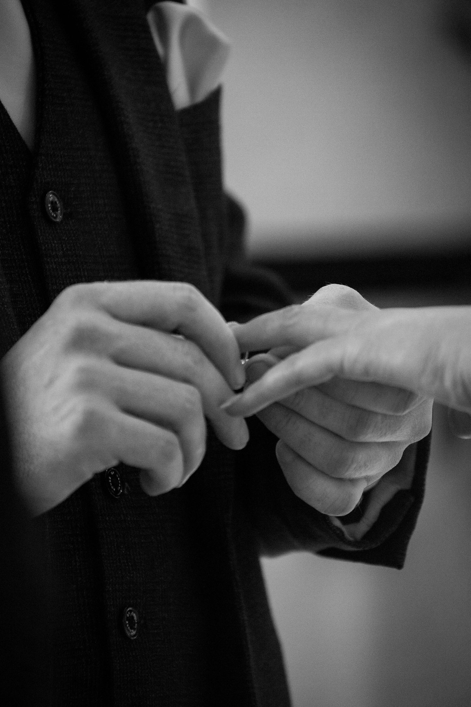 Black and white close-up of hands exchanging rings during a ceremony.