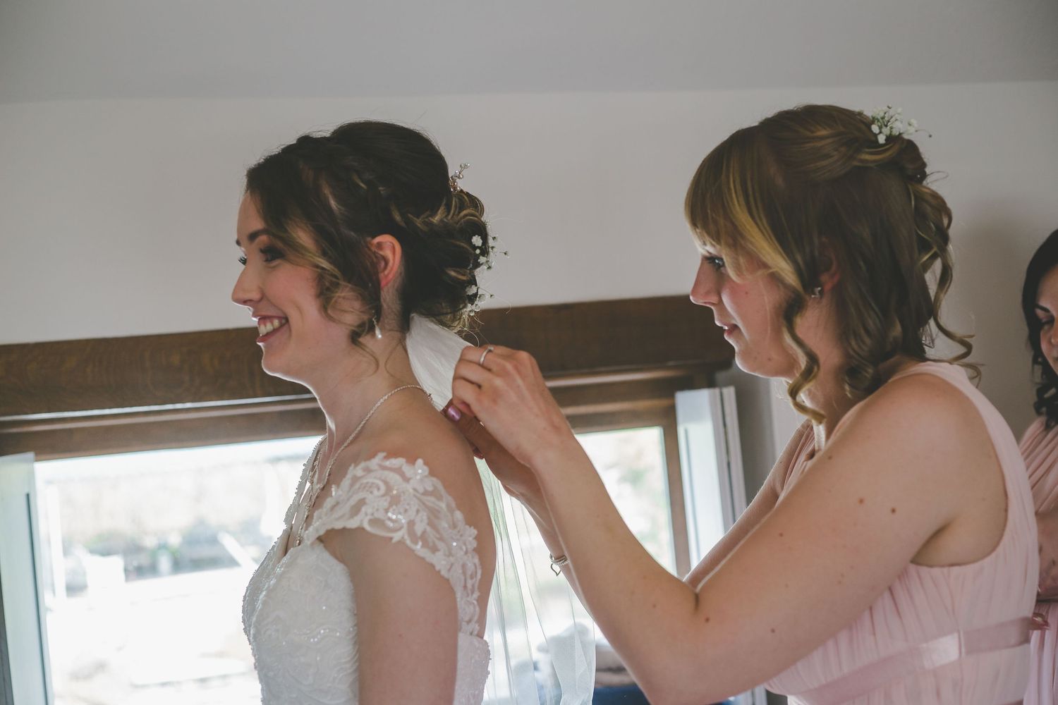 A bride and bridesmaids getting ready for a wedding in a bright room with natural light streaming through windows.