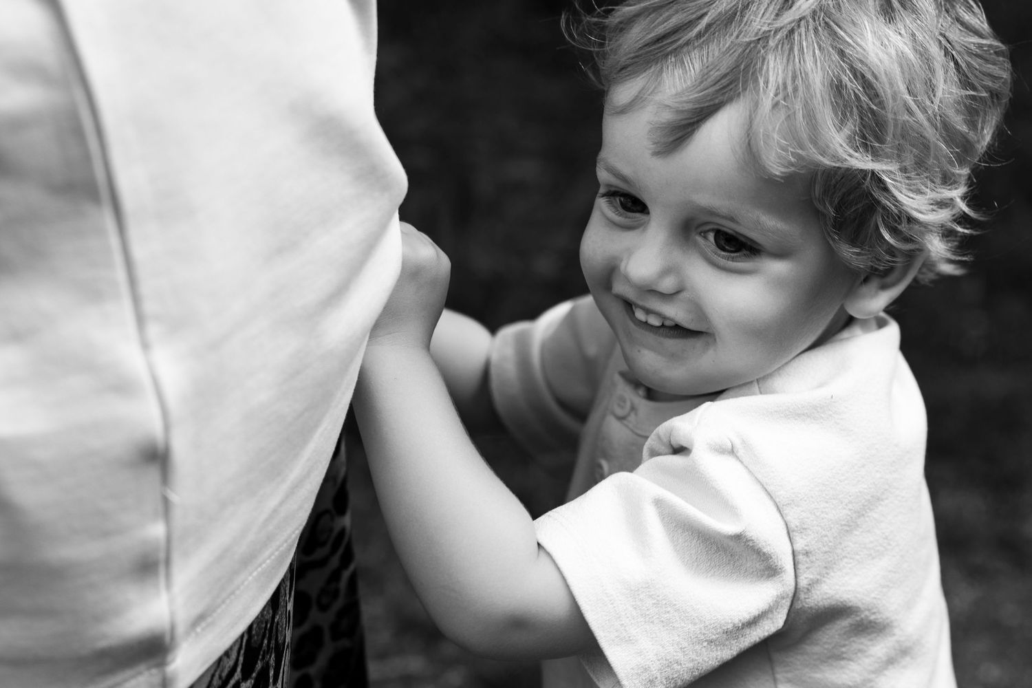 Black and white family photograph showing child holding onto his mother's clothing. Captures connection and real family moment.
