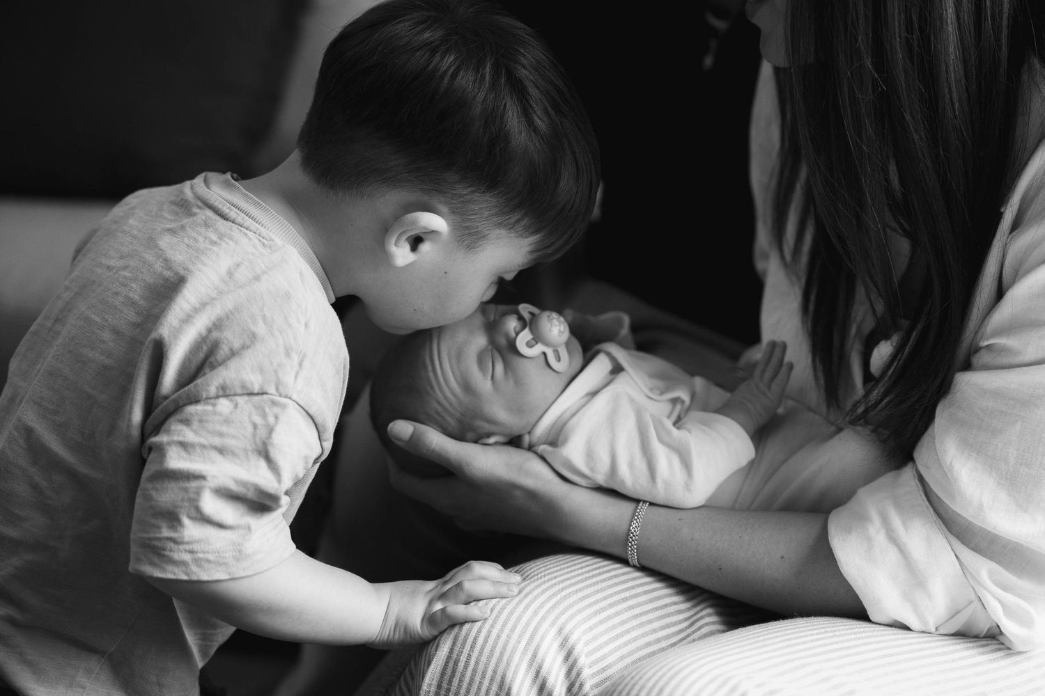 Newborn photograph of baby with older brother and mother, showing a tender real moment at an at-home session