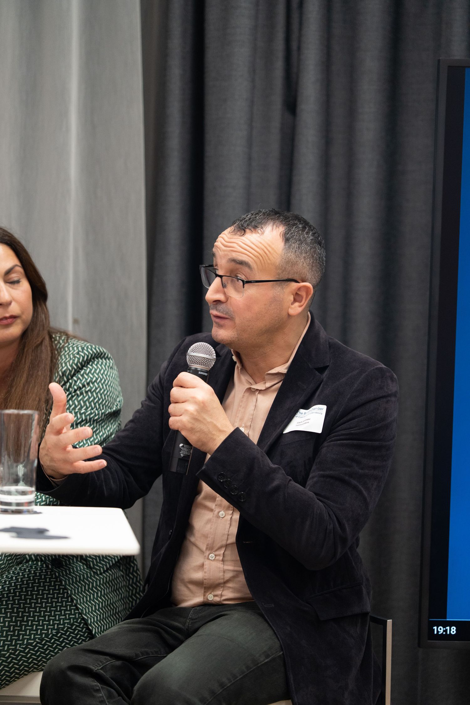 Man speaking into a microphone during a panel discussion at a professional business event.