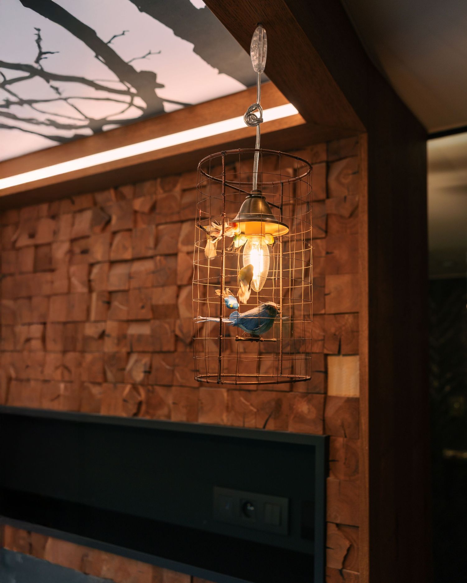 Decorative wire cage pendant light with bird figurine hanging against a rustic stone brick wall.