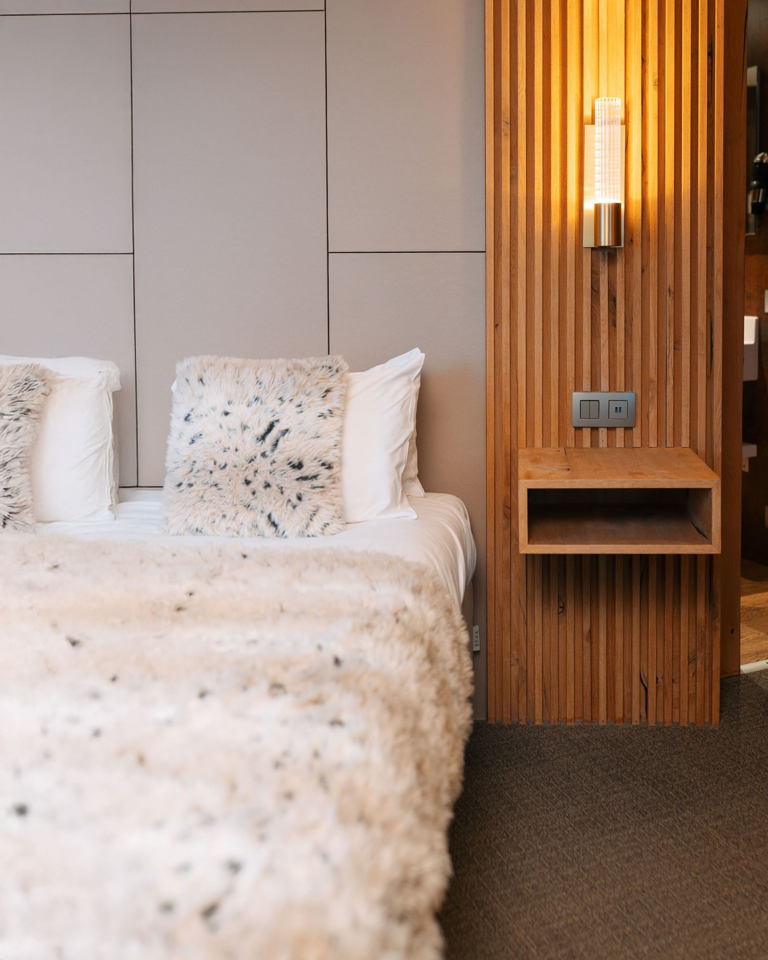 Cozy hotel bedroom with fluffy white pillows, textured blanket, and warm wooden bedside lighting.