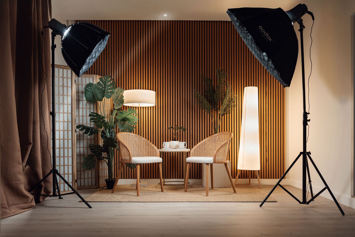 Professional photo studio setup with softbox lights, wicker chairs, and wooden slat wall backdrop.