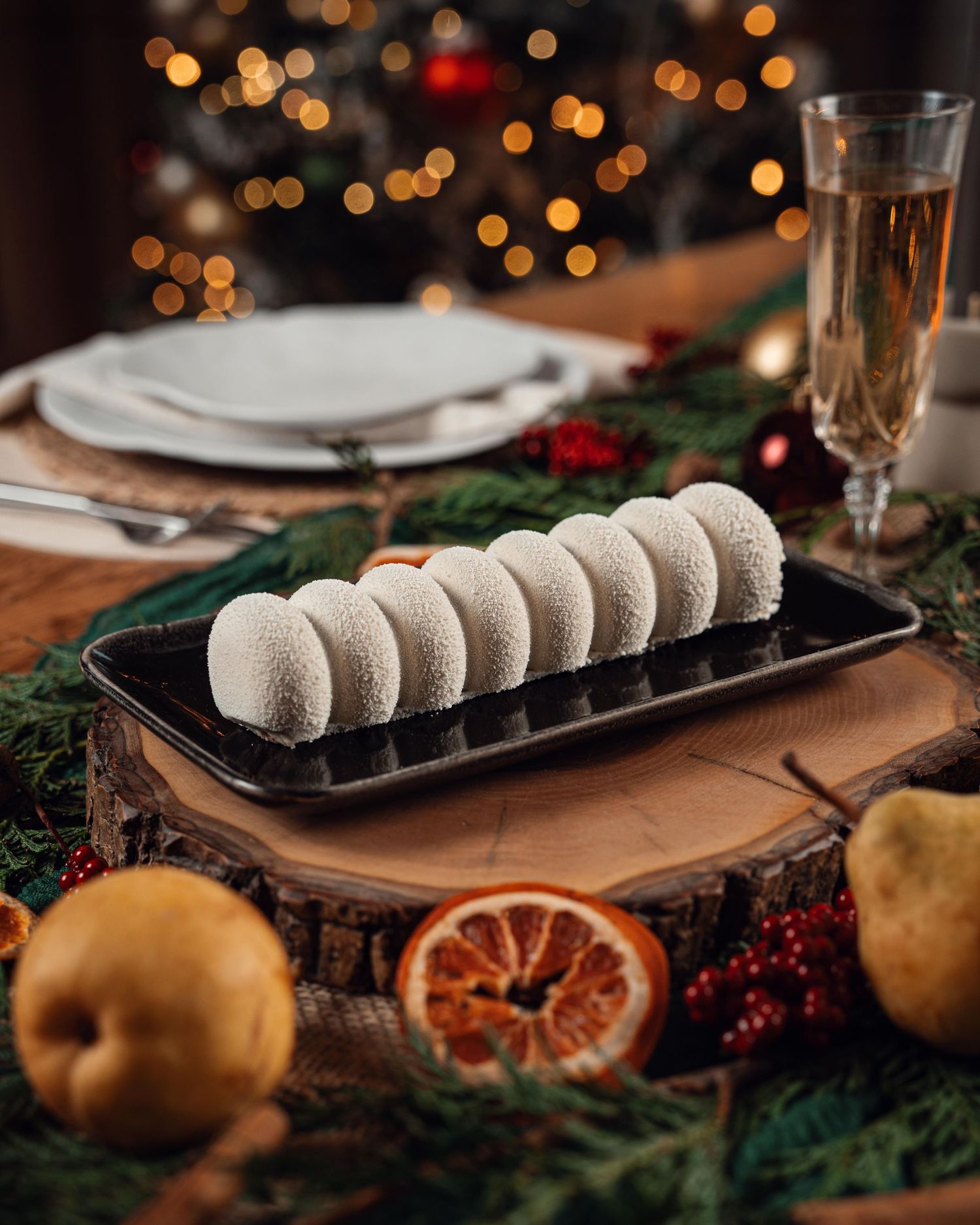 Elegant row of white coconut truffle desserts on black plate with festive Christmas table decor and champagne.