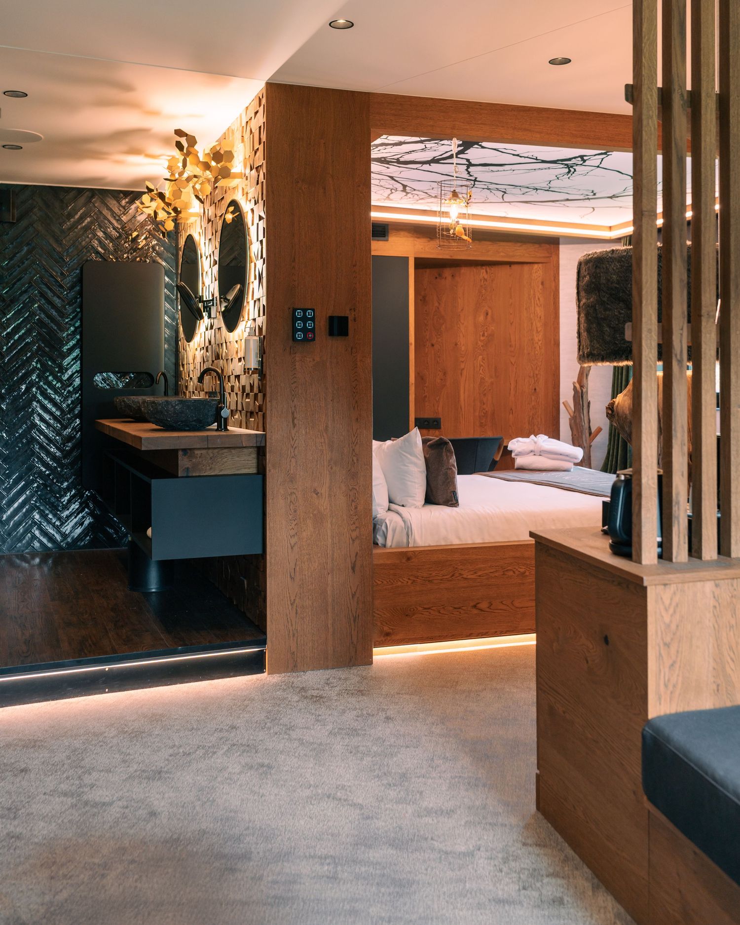 Luxurious hotel room with wooden accents, designer lighting, and elegant bathroom visible through partition.