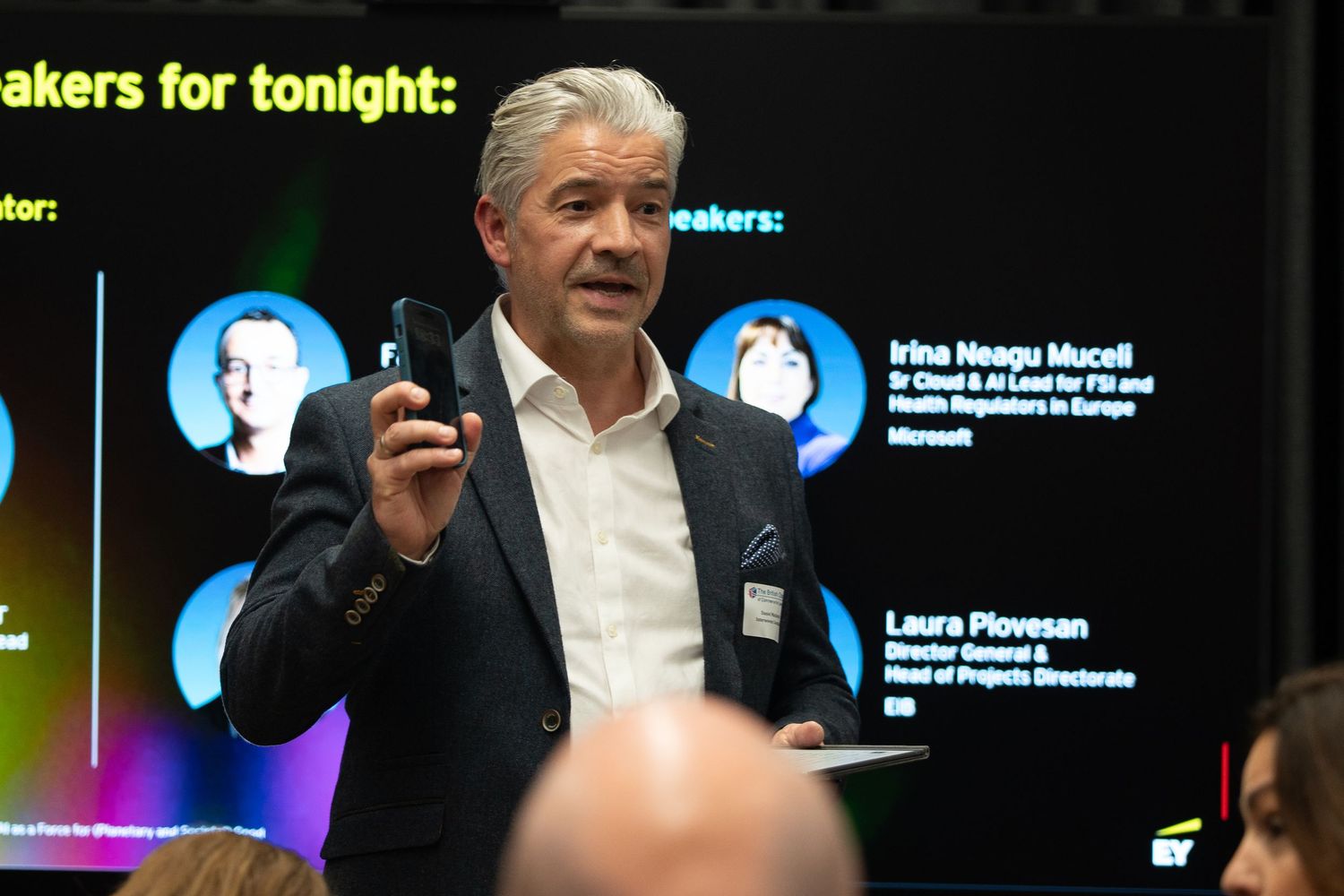 Male keynote speaker presenting at a corporate technology conference with speaker list displayed.