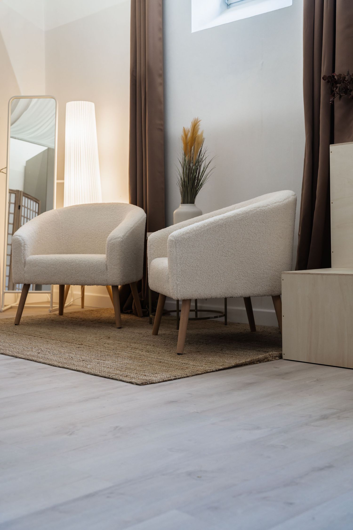 Two cream boucle armchairs on a jute rug in a modern living room with a floor lamp and tall mirror.