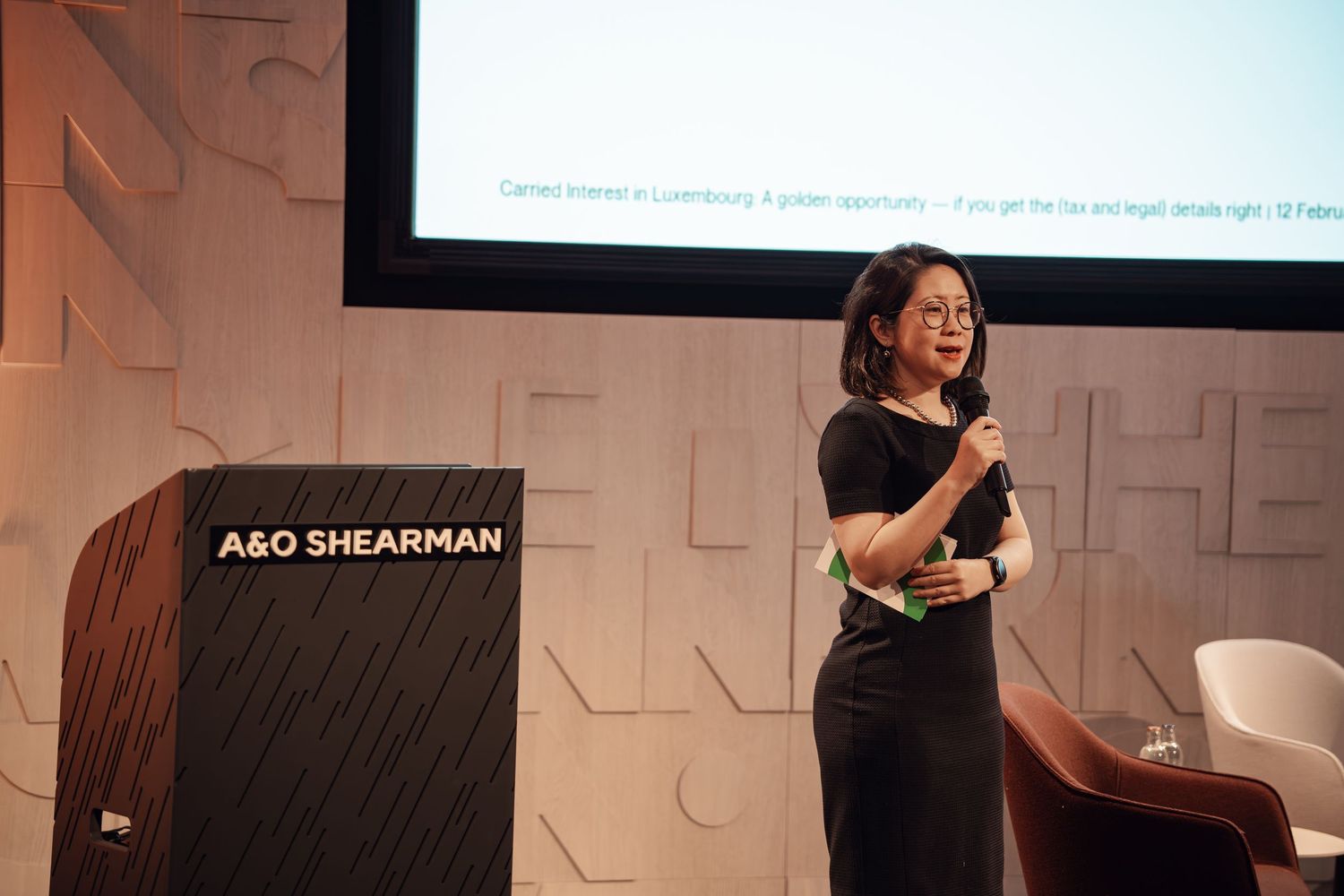 Female speaker presenting at A&O Shearman corporate event with projection screen.