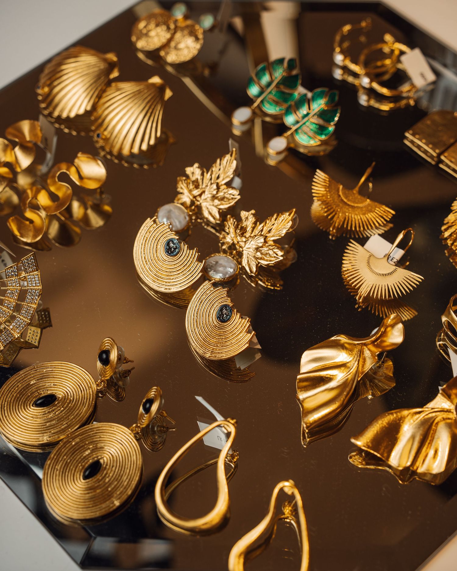 Collection of gold statement earrings displayed on dark reflective surface.