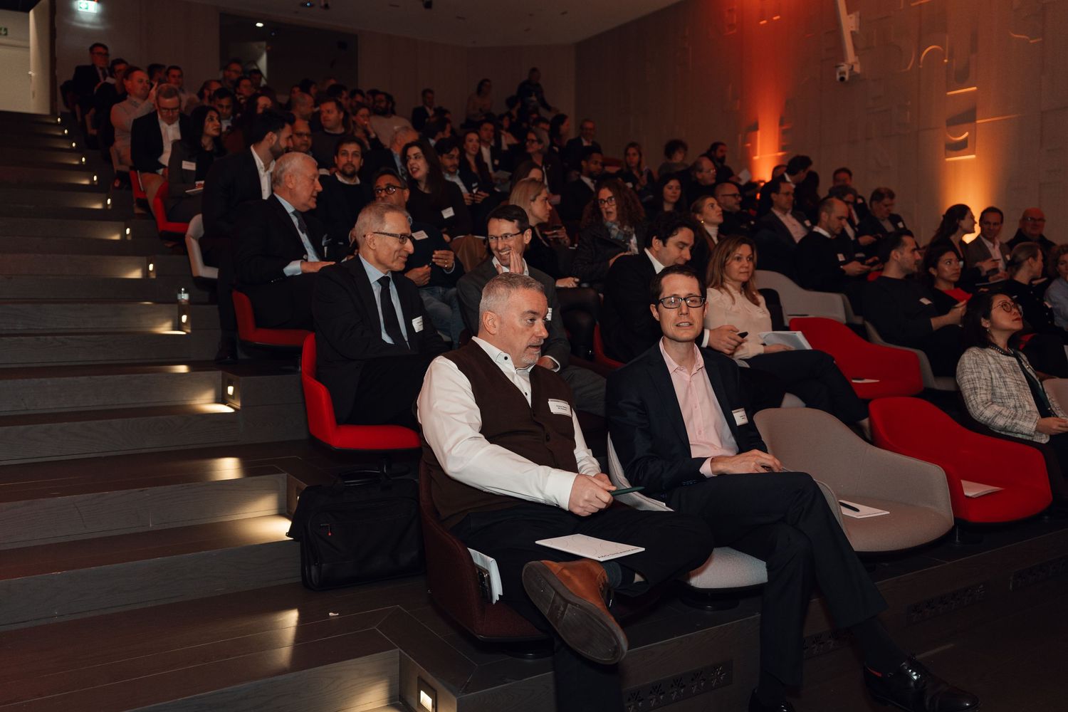 Audience of business professionals seated in tiered conference venue during corporate presentation.
