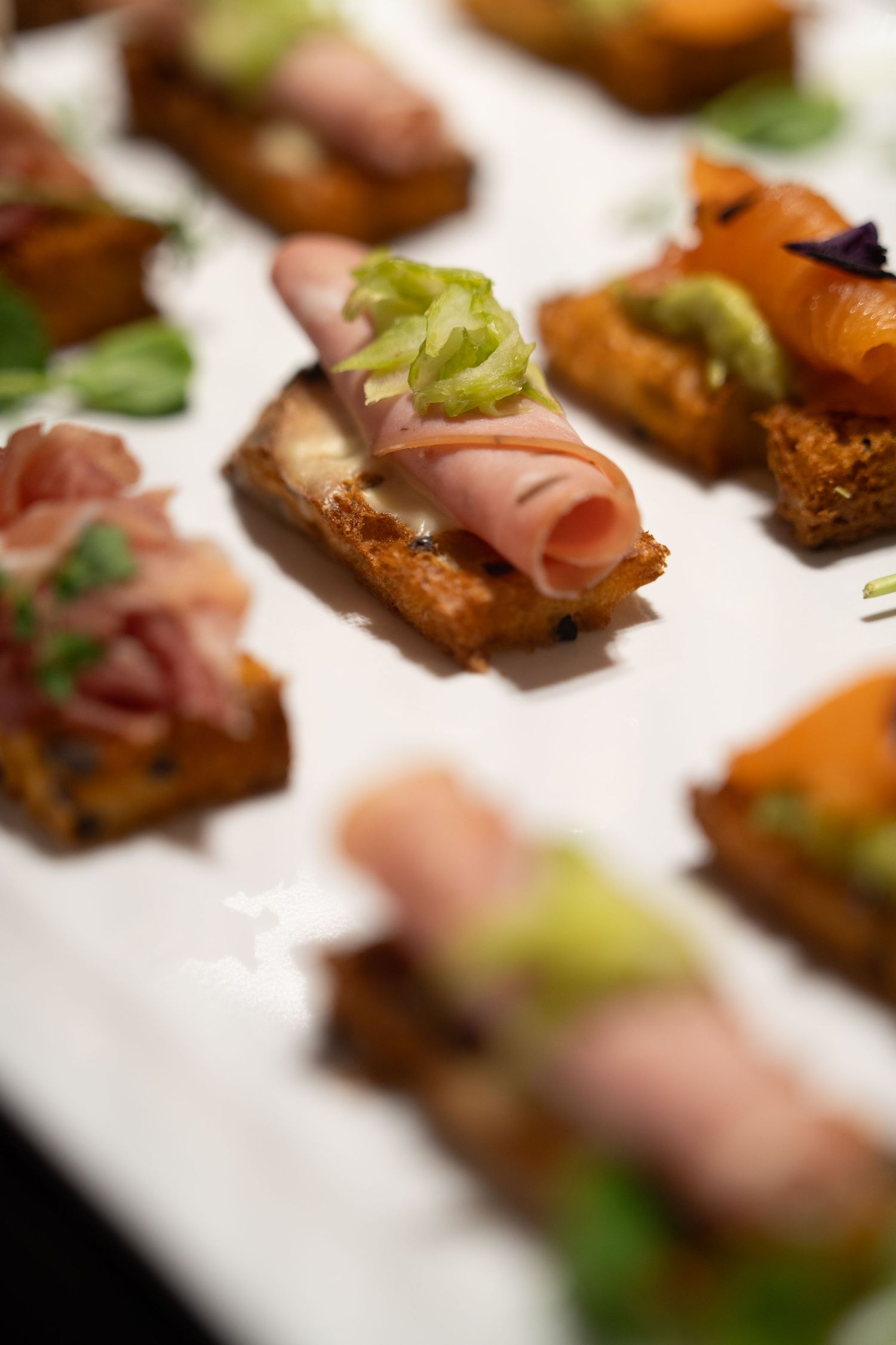 Elegant canapés with ham and garnishes served on a white platter at a catering event.