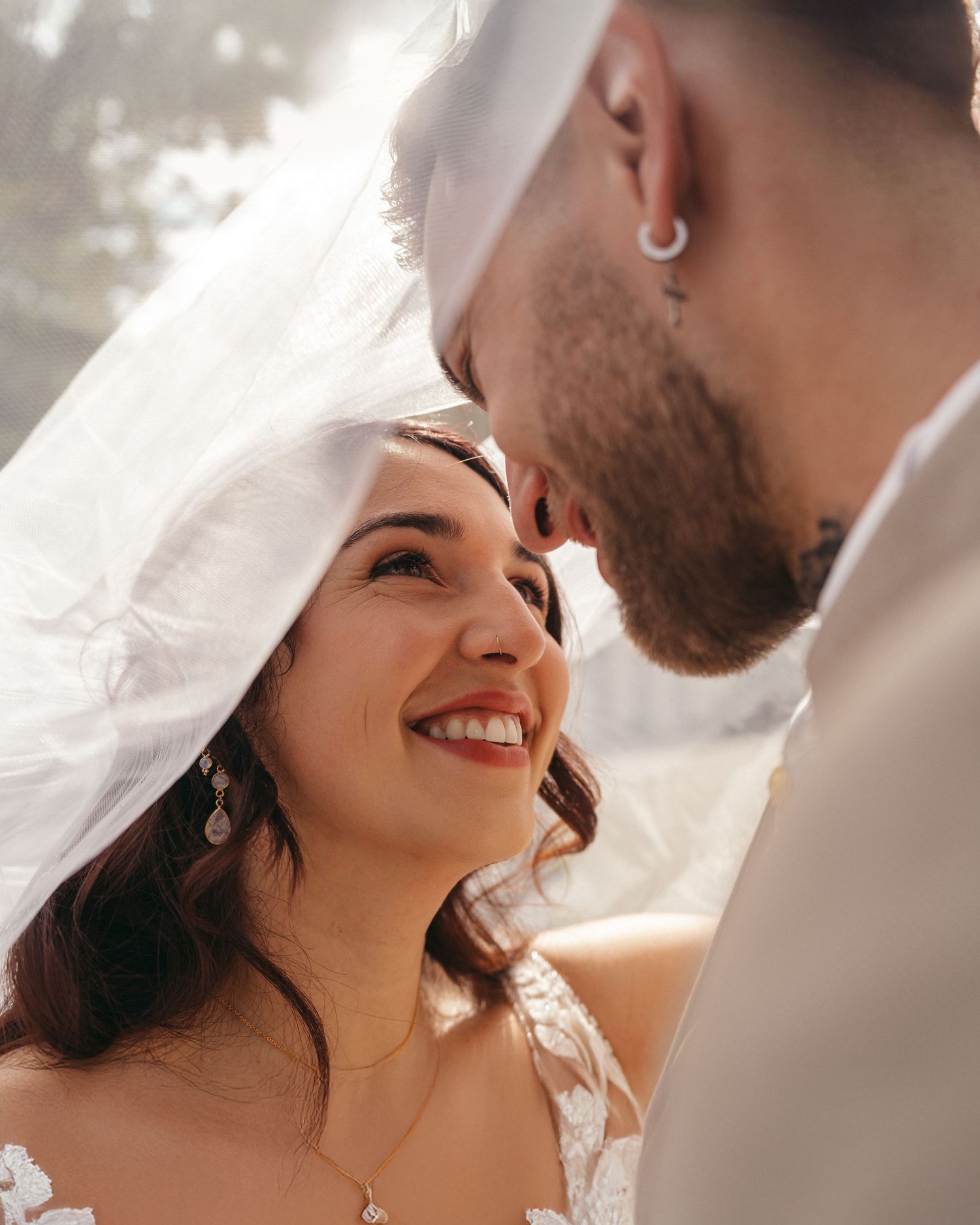 A joyful bride smiles up at her groom during a romantic wedding moment, with her veil softly framing the scene.