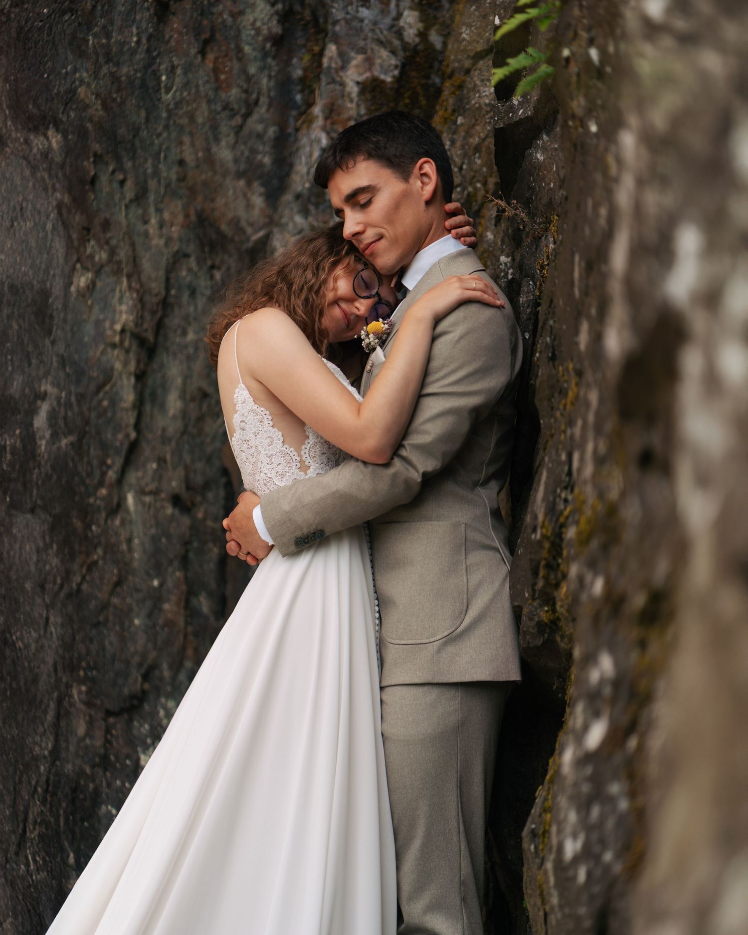 Bride and groom embracing tenderly against a rocky natural stone wall backdrop.