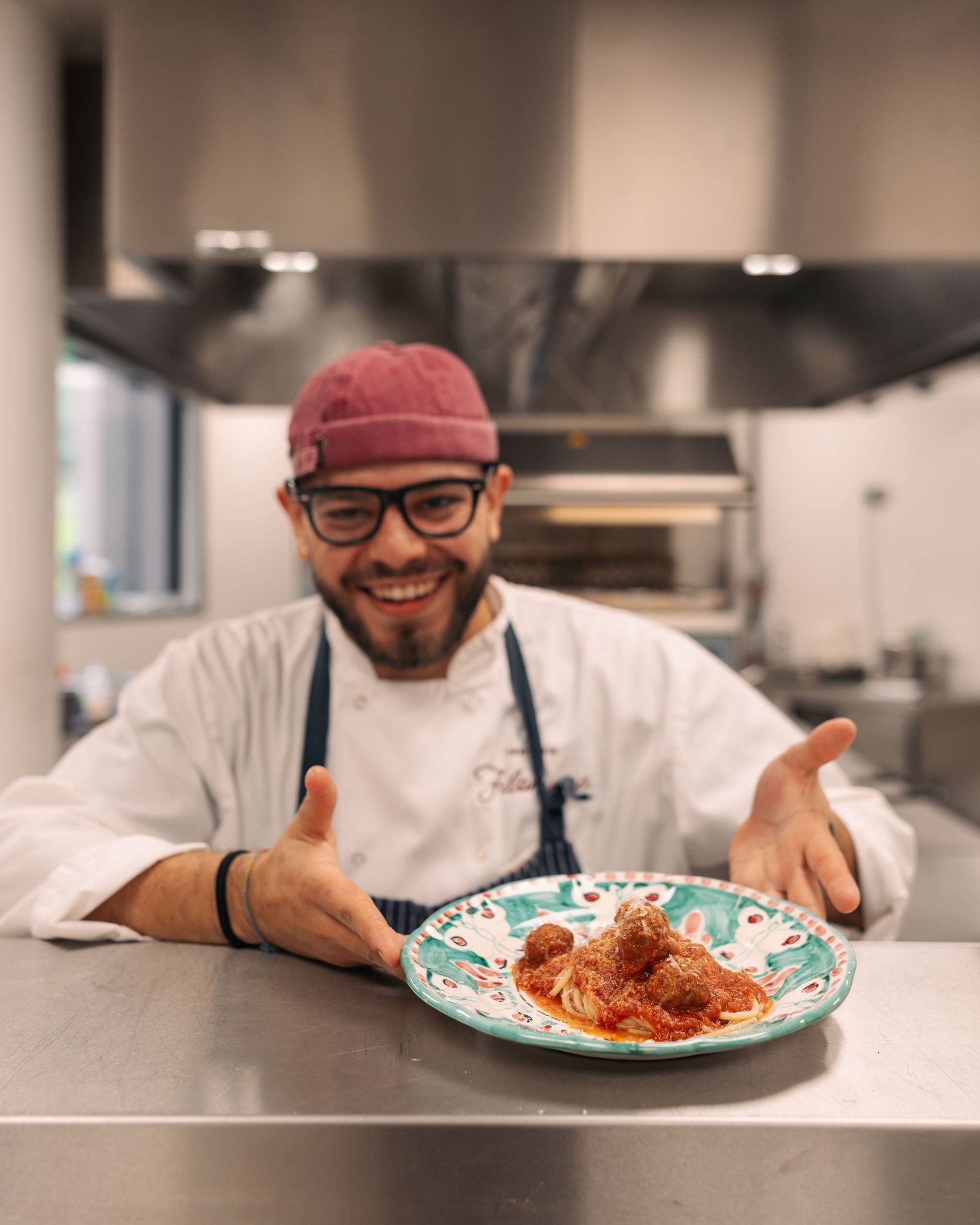 Smiling chef presenting plate of spaghetti and meatballs in professional kitchen.