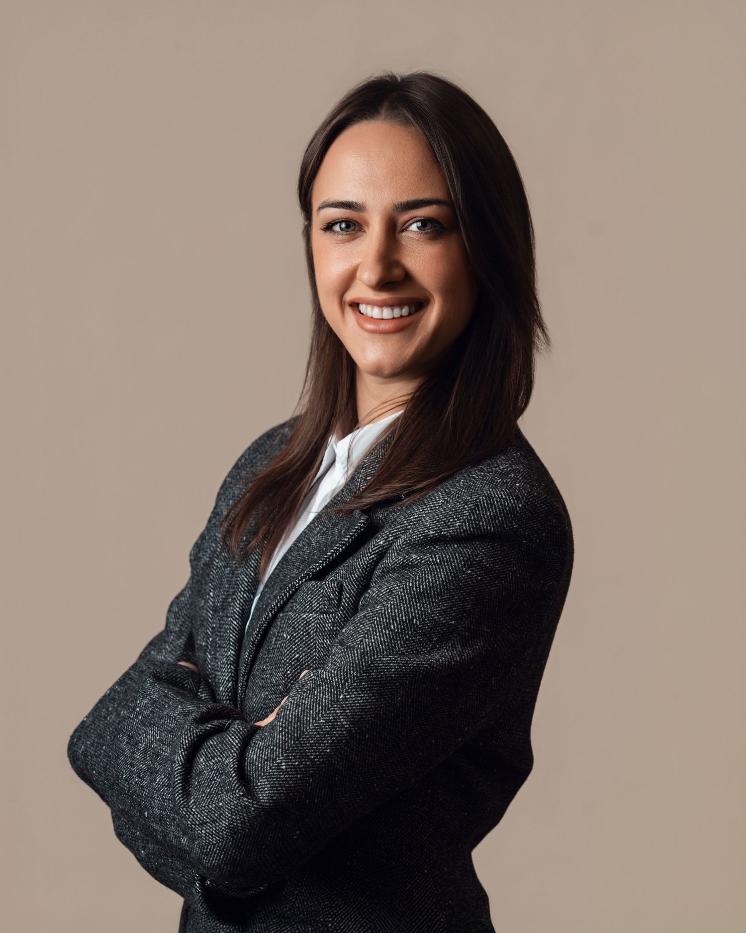 Smiling professional woman in a dark blazer with arms crossed against a neutral beige background.