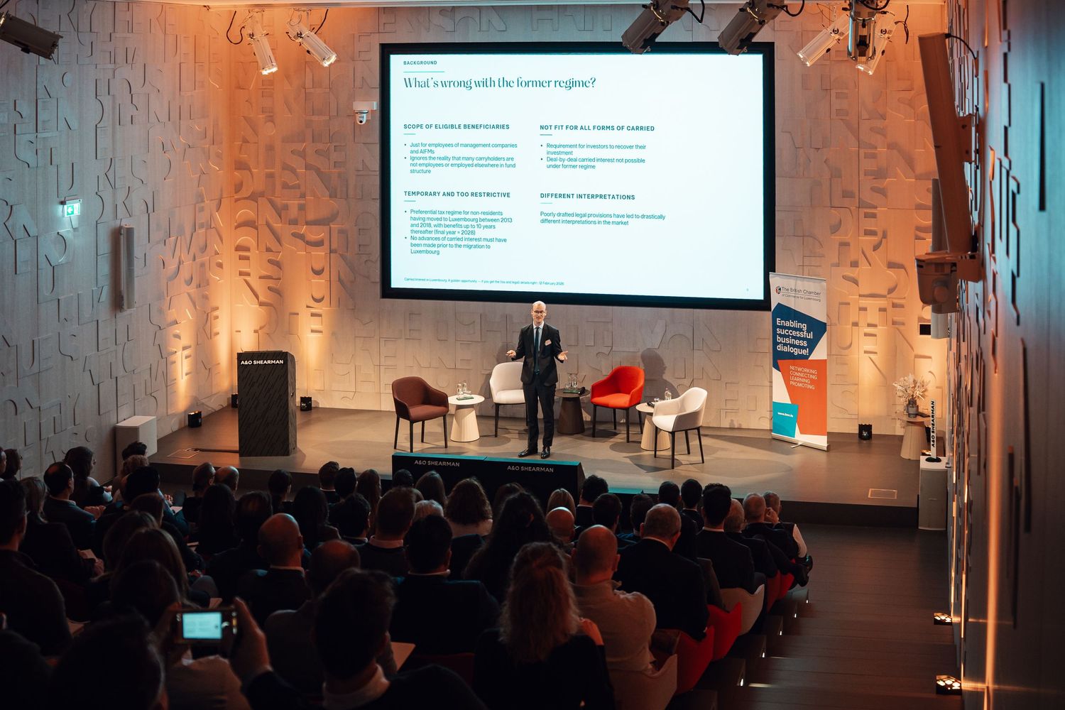 Speaker presenting to large audience at A&O Shearman corporate conference hall.