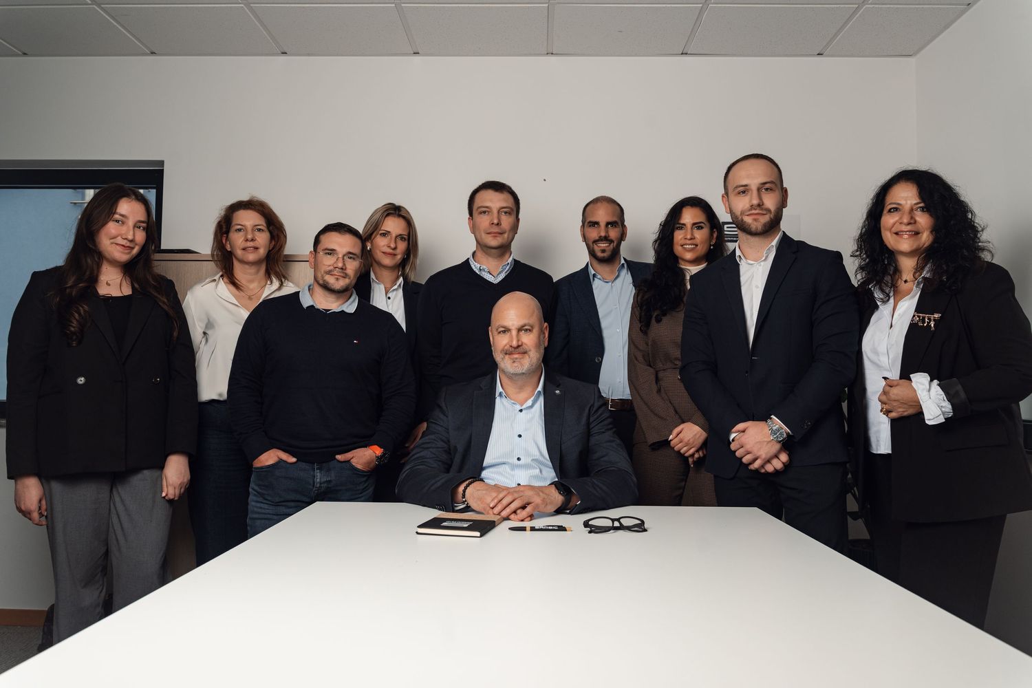 Professional business team of nine people posing together in a modern office conference room.