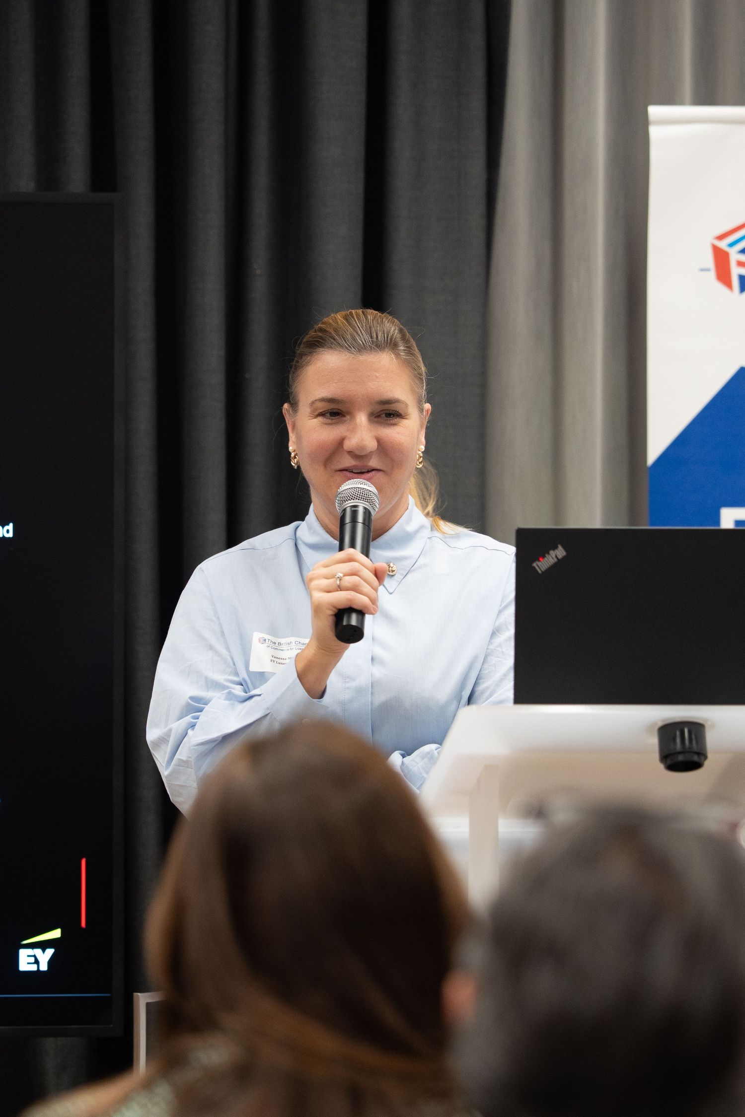 Smiling young woman speaking into a microphone at a corporate EY conference event.