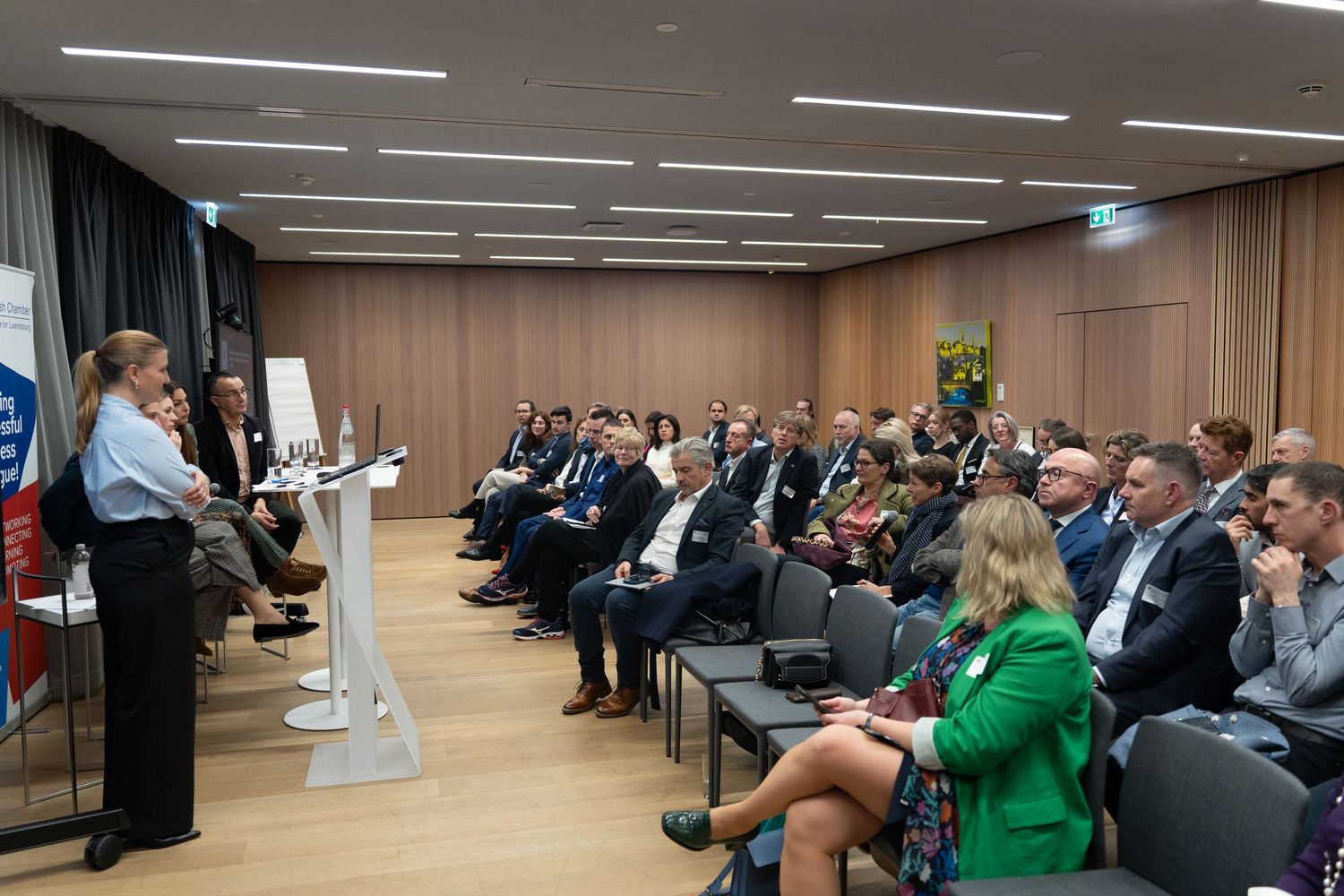 Professional conference presentation with speaker at podium addressing large seated audience in modern meeting room.