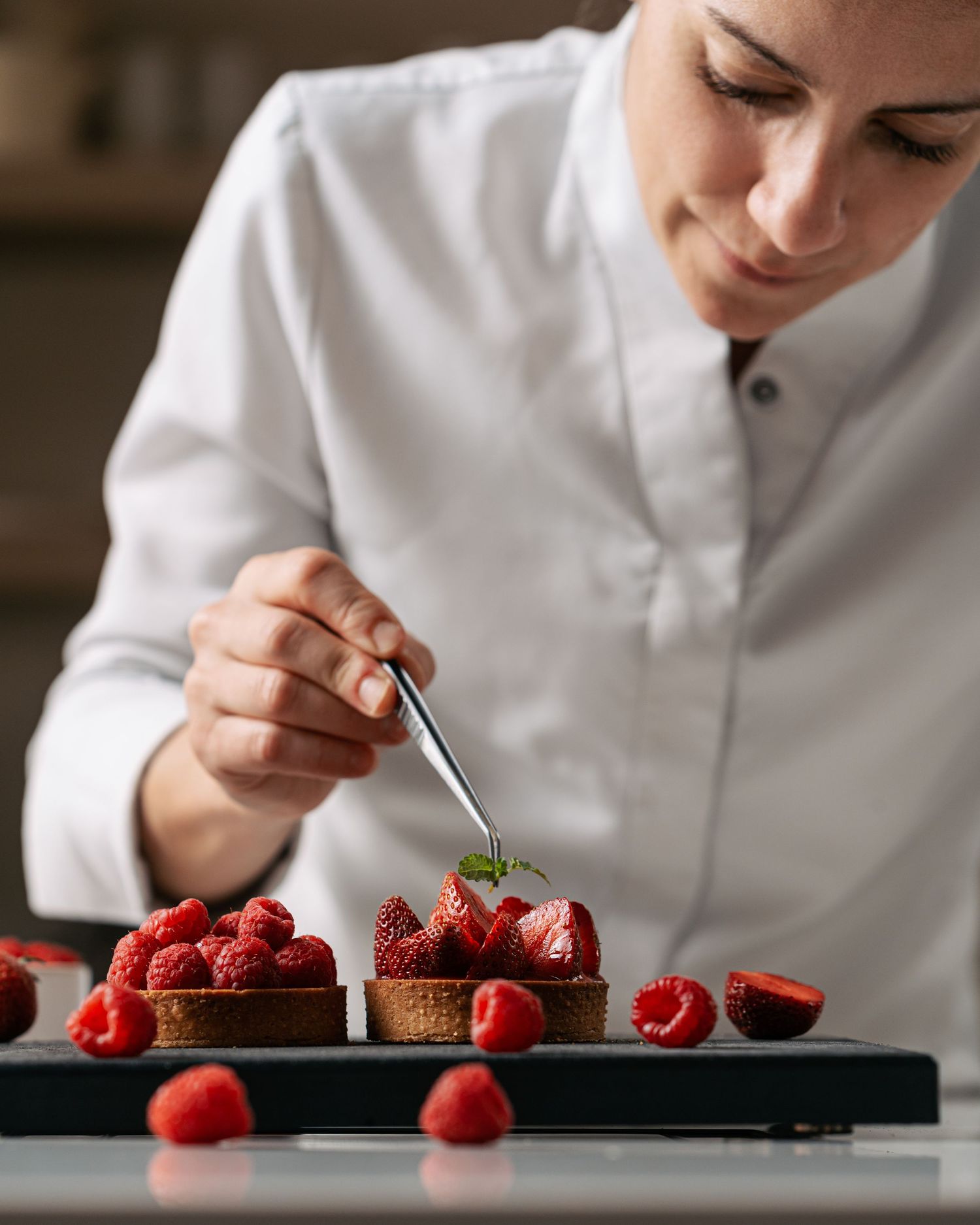 Female pastry chef using tweezers to plate a mint garnish on a berry tart.