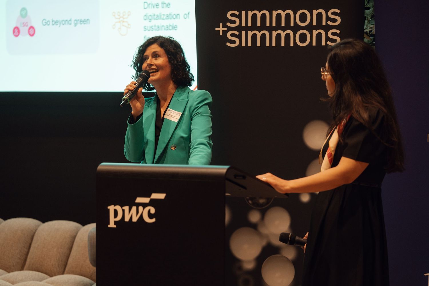 Two women present on stage at a PwC and Simmons Simmons corporate event.