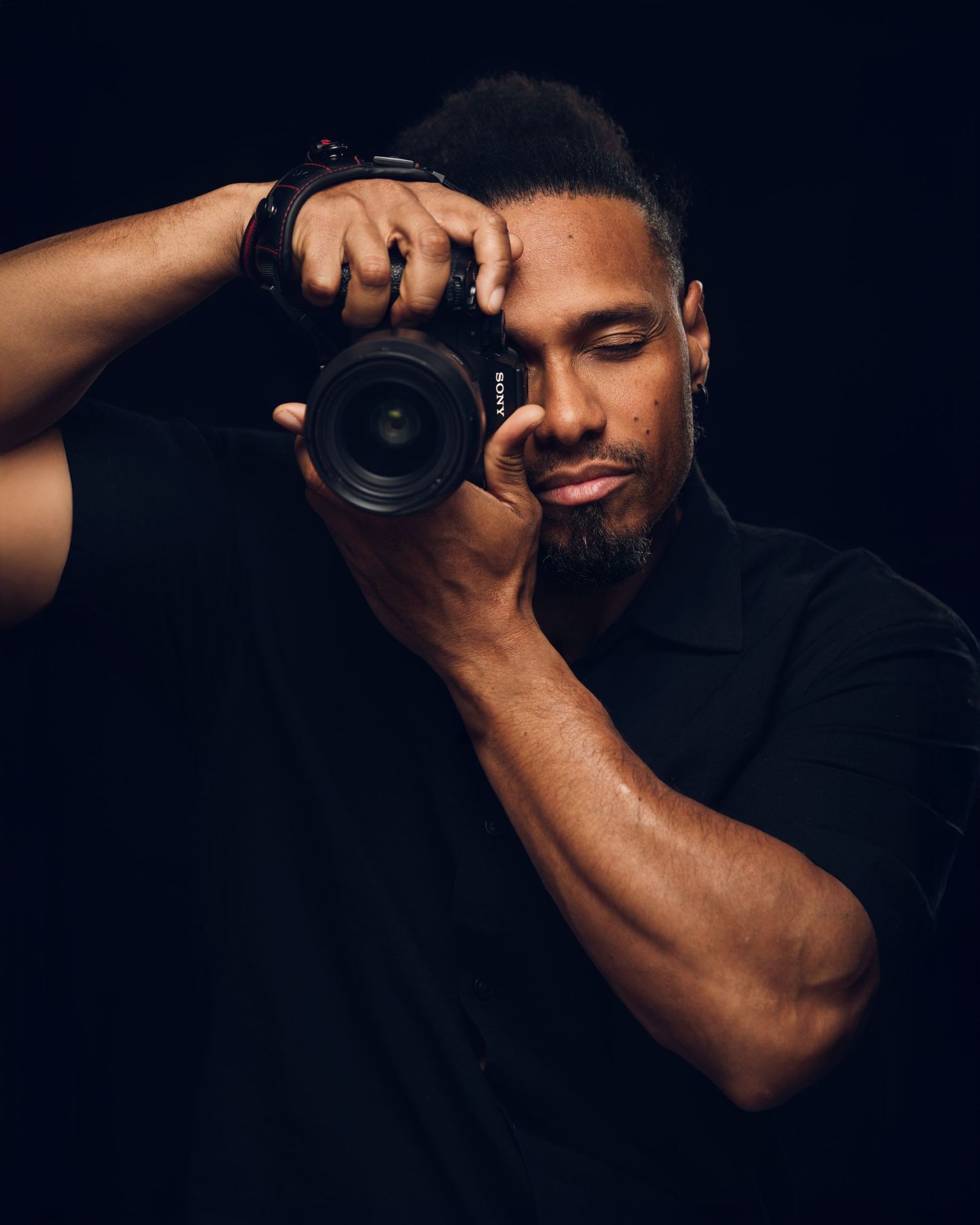 A focused male photographer holds up a Canon DSLR camera to shoot against a dark background.