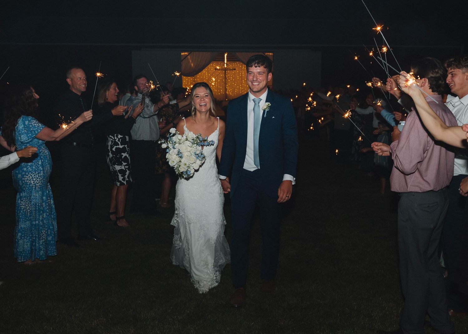 A newlywed couple walks through sparklers at night during their wedding reception celebration.