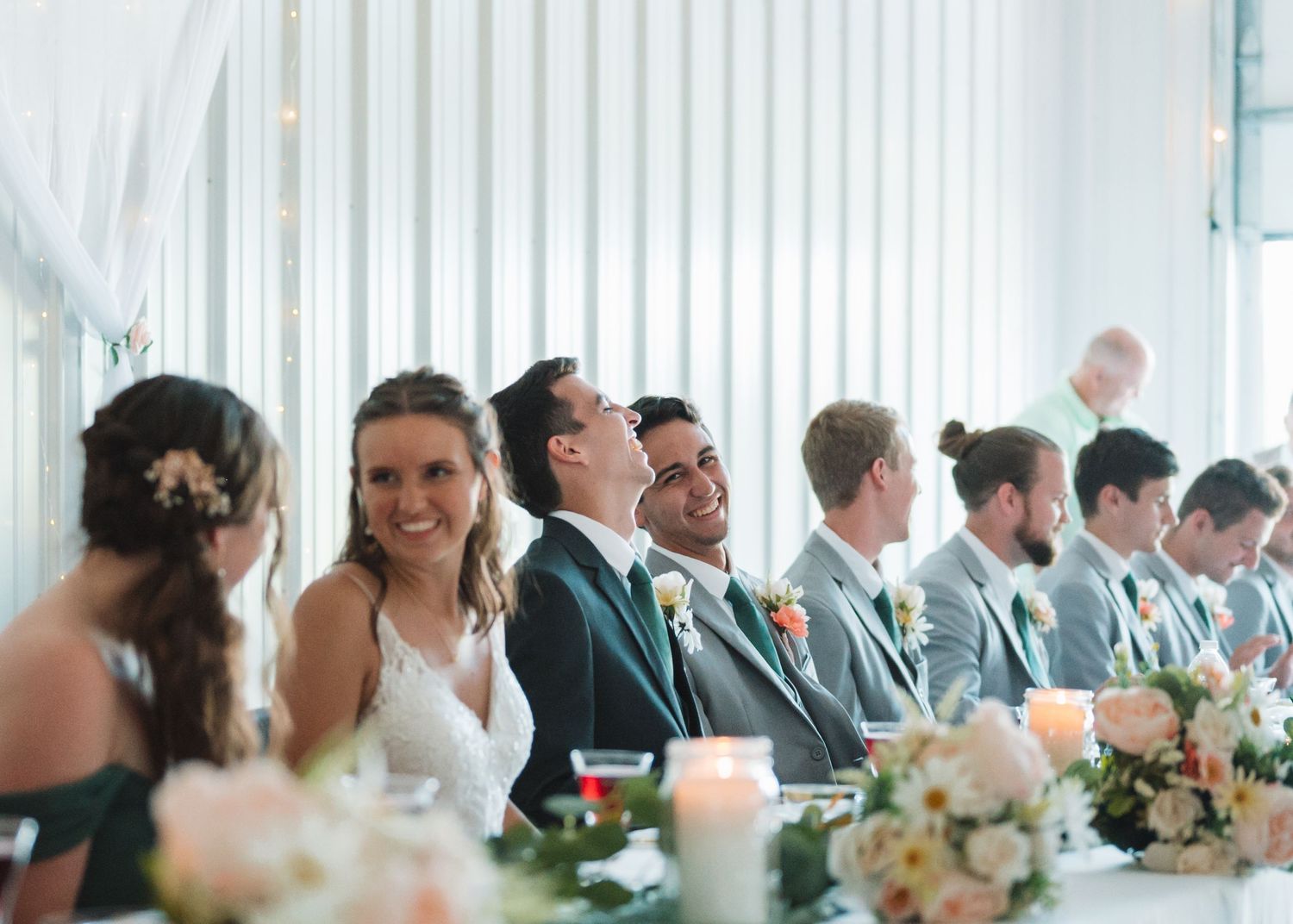 Wedding party seated at long reception tables decorated with floral centerpieces.
