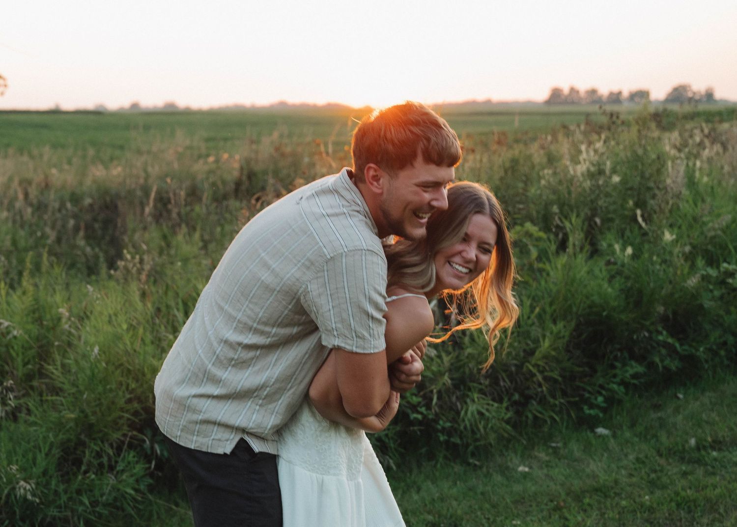 A couple embraces in a romantic moment at sunset in a grassy meadow during golden hour.