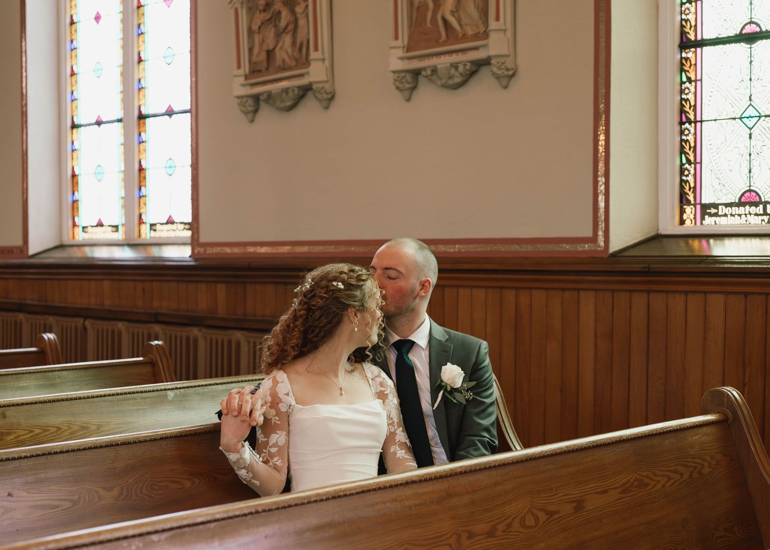 Church interior with wooden pews and stained glass windows during a wedding ceremony.