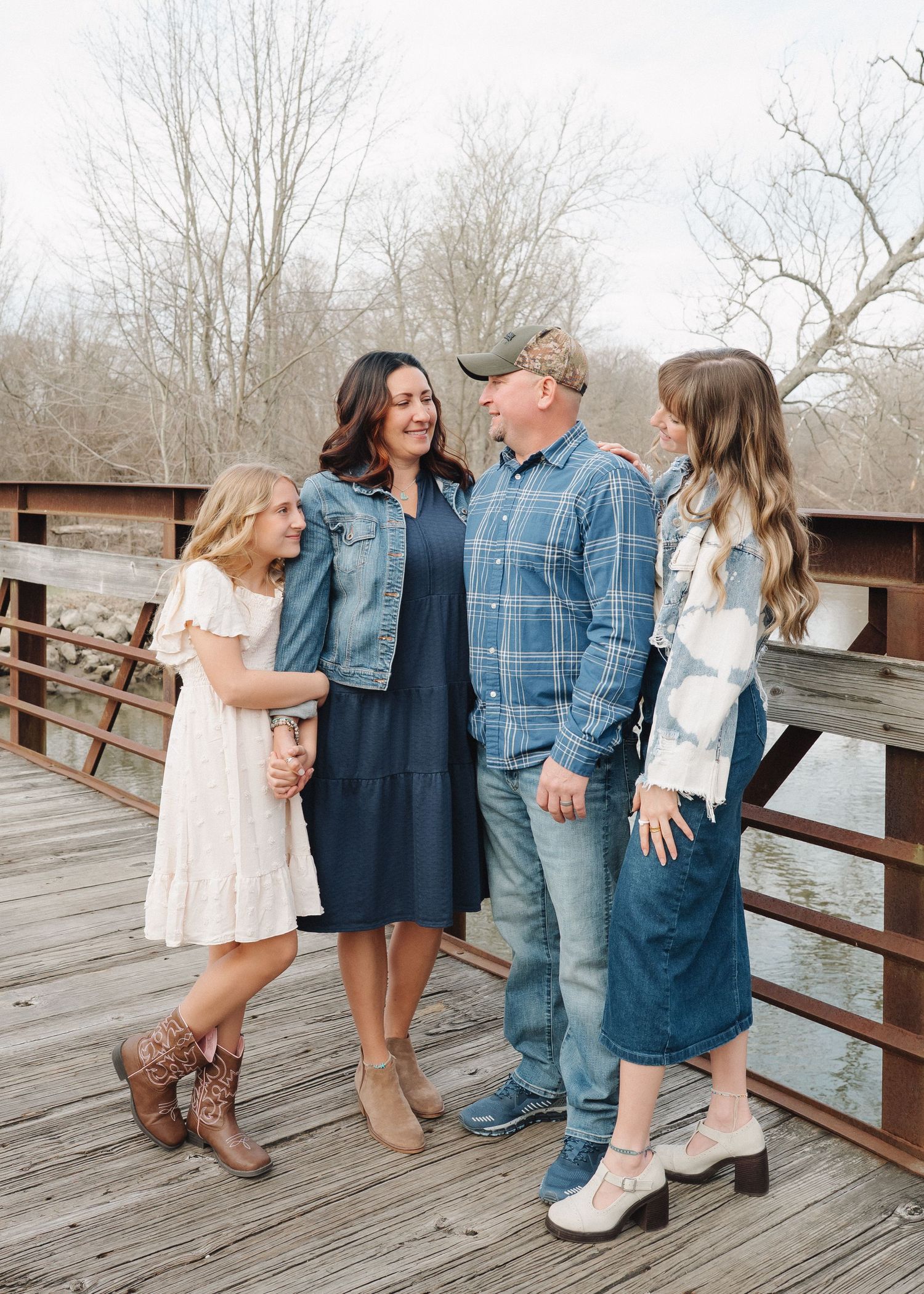 A group poses together on a wooden bridge wearing coordinated casual outfits in denim and neutral colors.