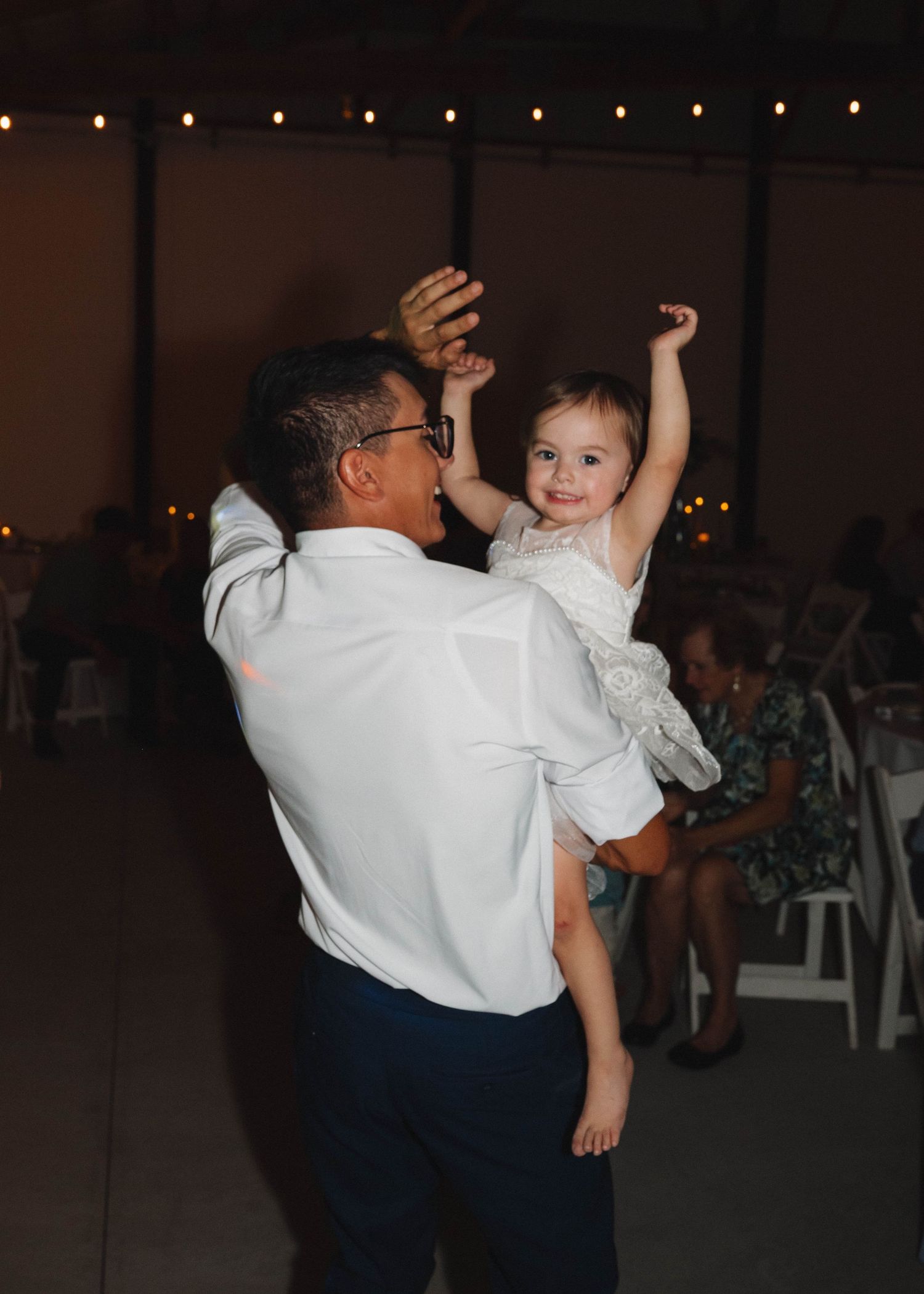 People dancing together at an indoor celebration with string lights decorating the venue ceiling.