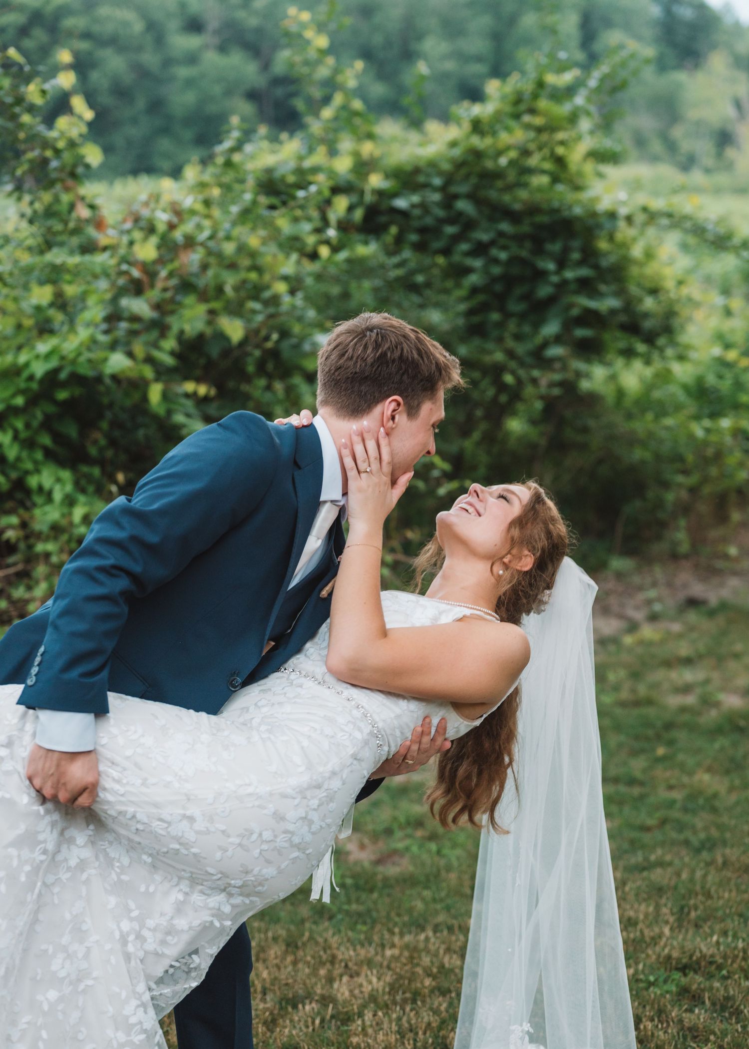 Romantic couple in wedding attire share a dramatic dip kiss pose in a lush garden setting.