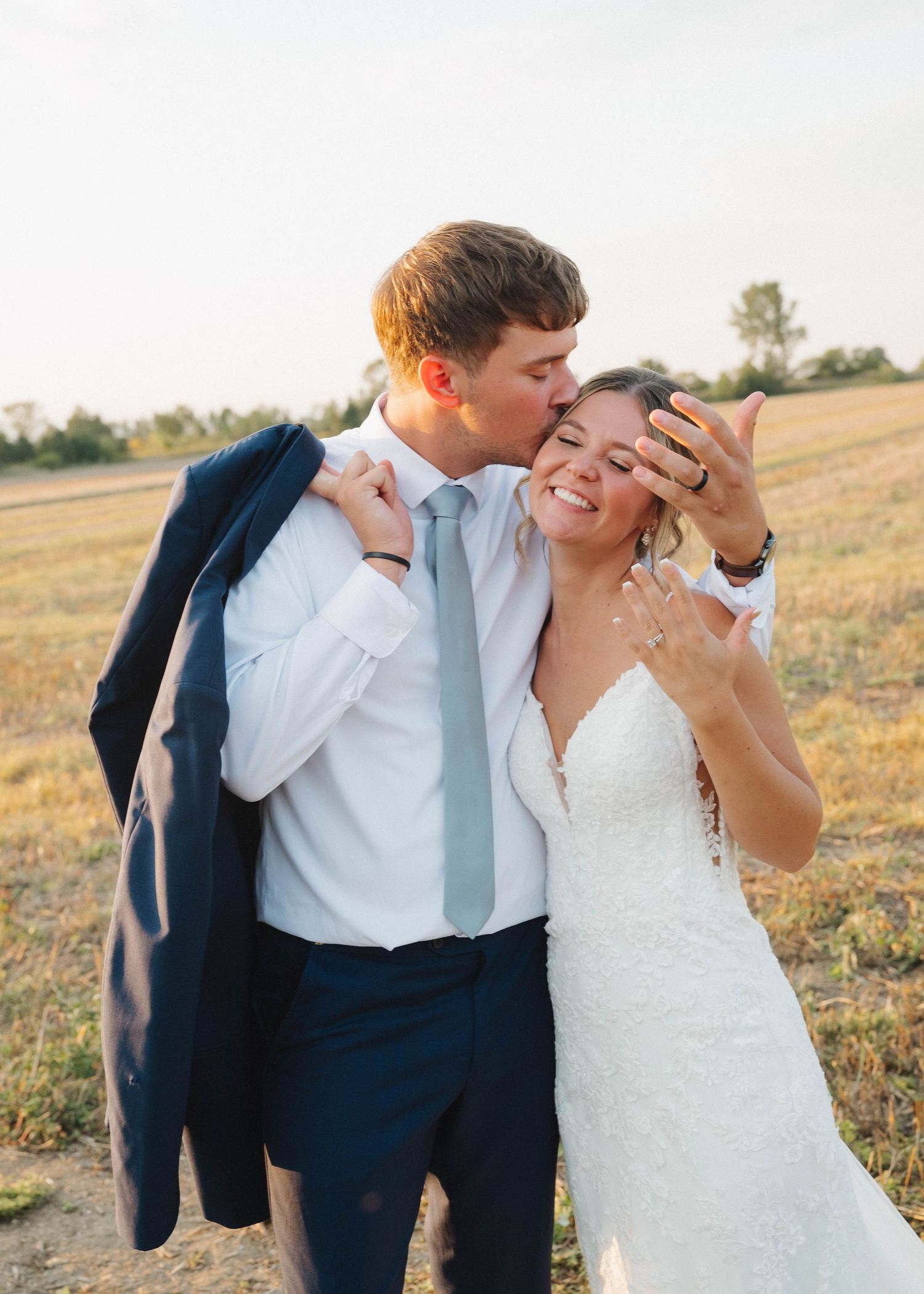 A romantic couple shares tender moments in a golden field at sunset wearing wedding attire.