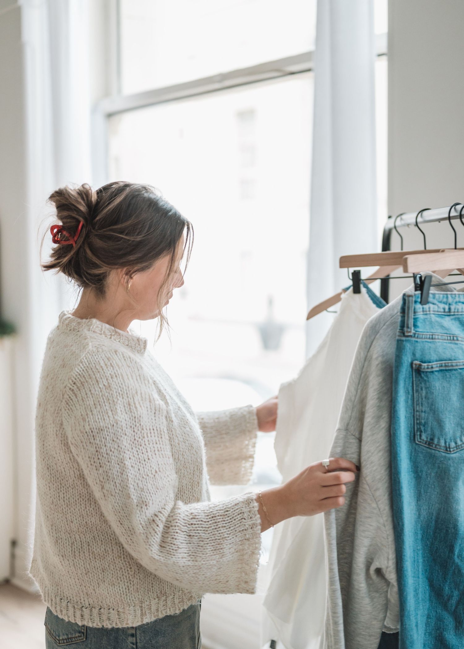 Person organizing white and denim clothing items on retail display racks near bright windows.