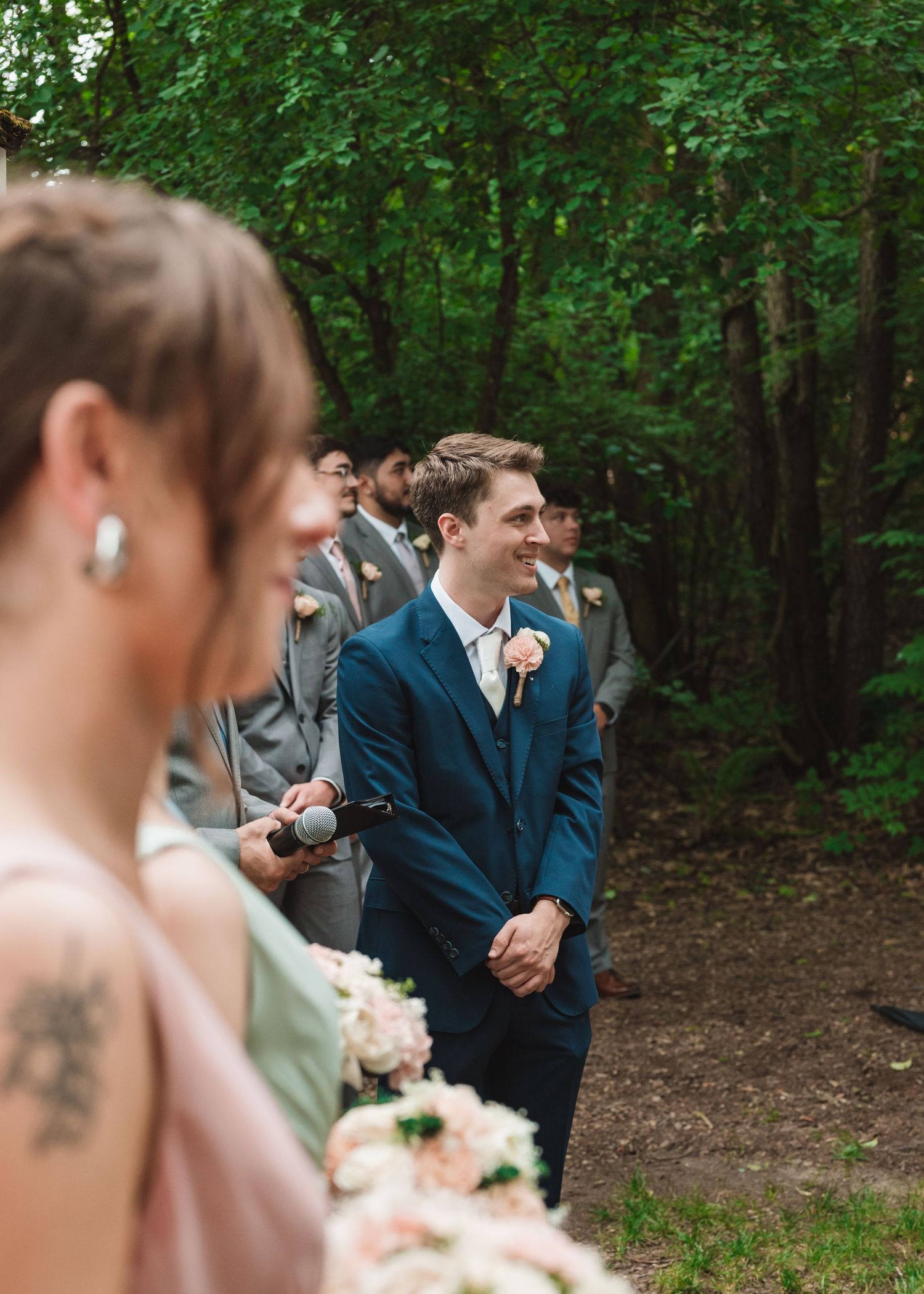 Wedding party members stand in a wooded setting during the ceremony.