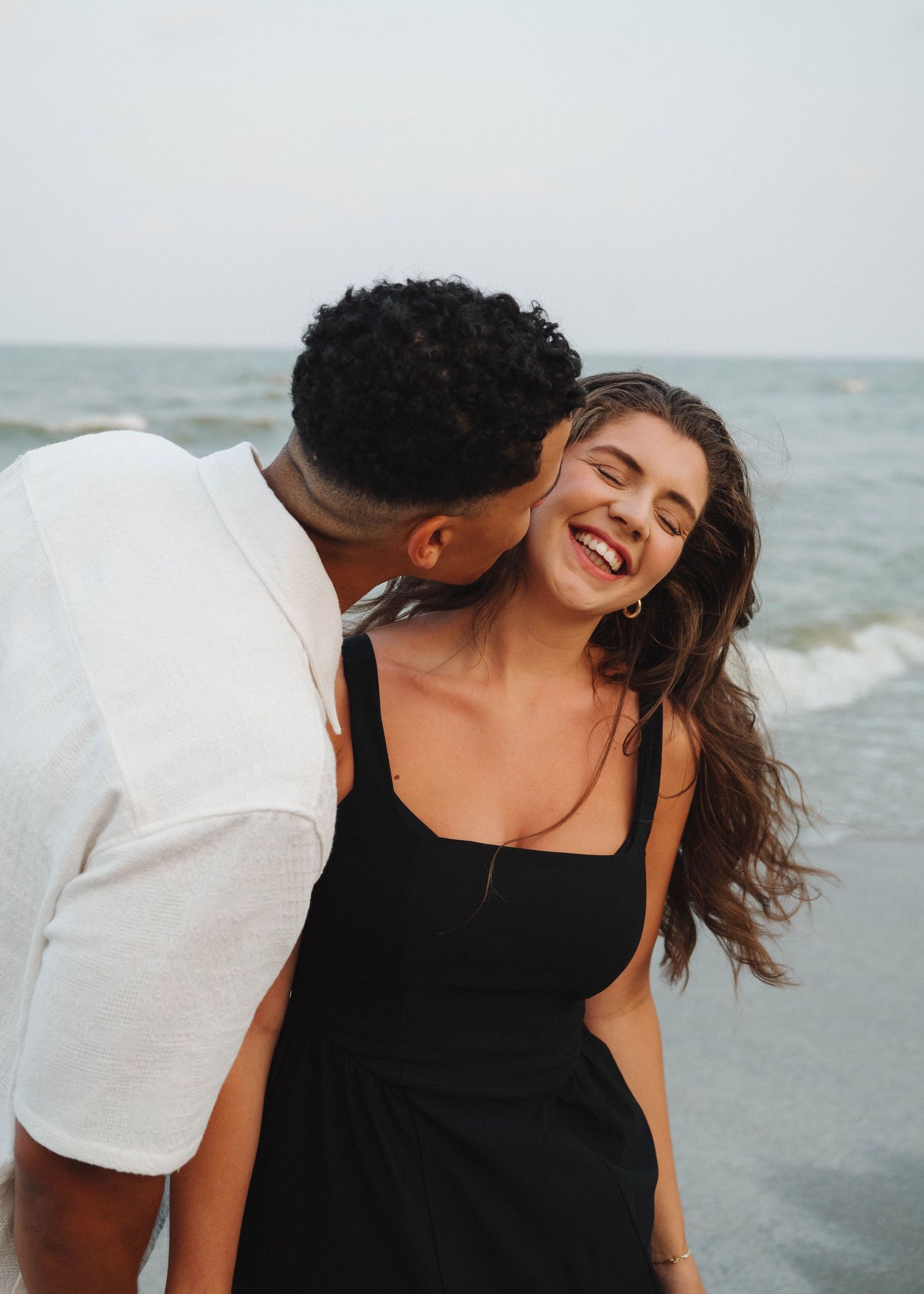 A couple shares a joyful moment at the beach with the ocean waves in the background.