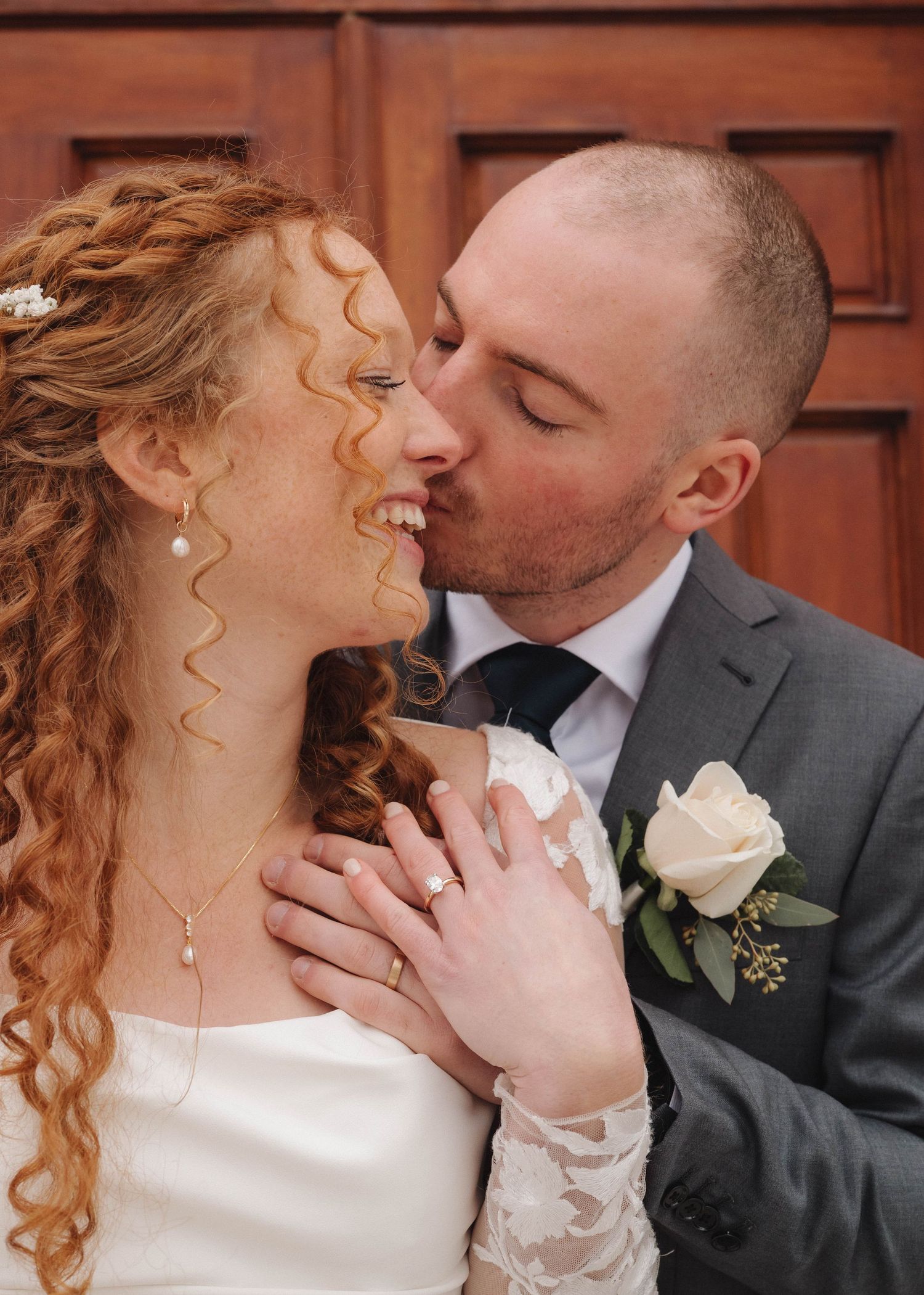 Wedding couple sharing tender kisses in front of rustic brick backdrop.
