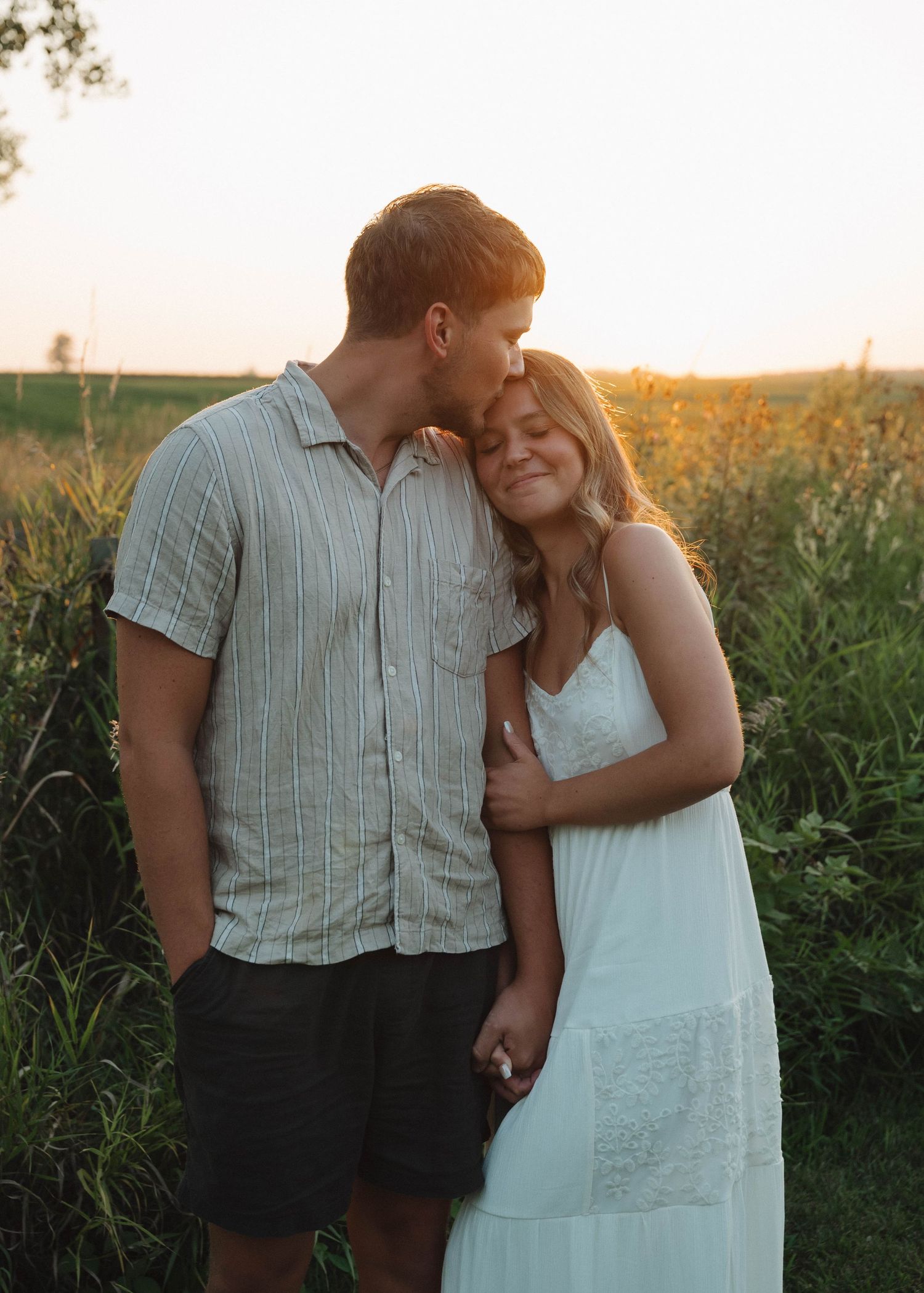 A couple embraces tenderly in a cornfield at sunset, creating a romantic silhouette against the golden light.