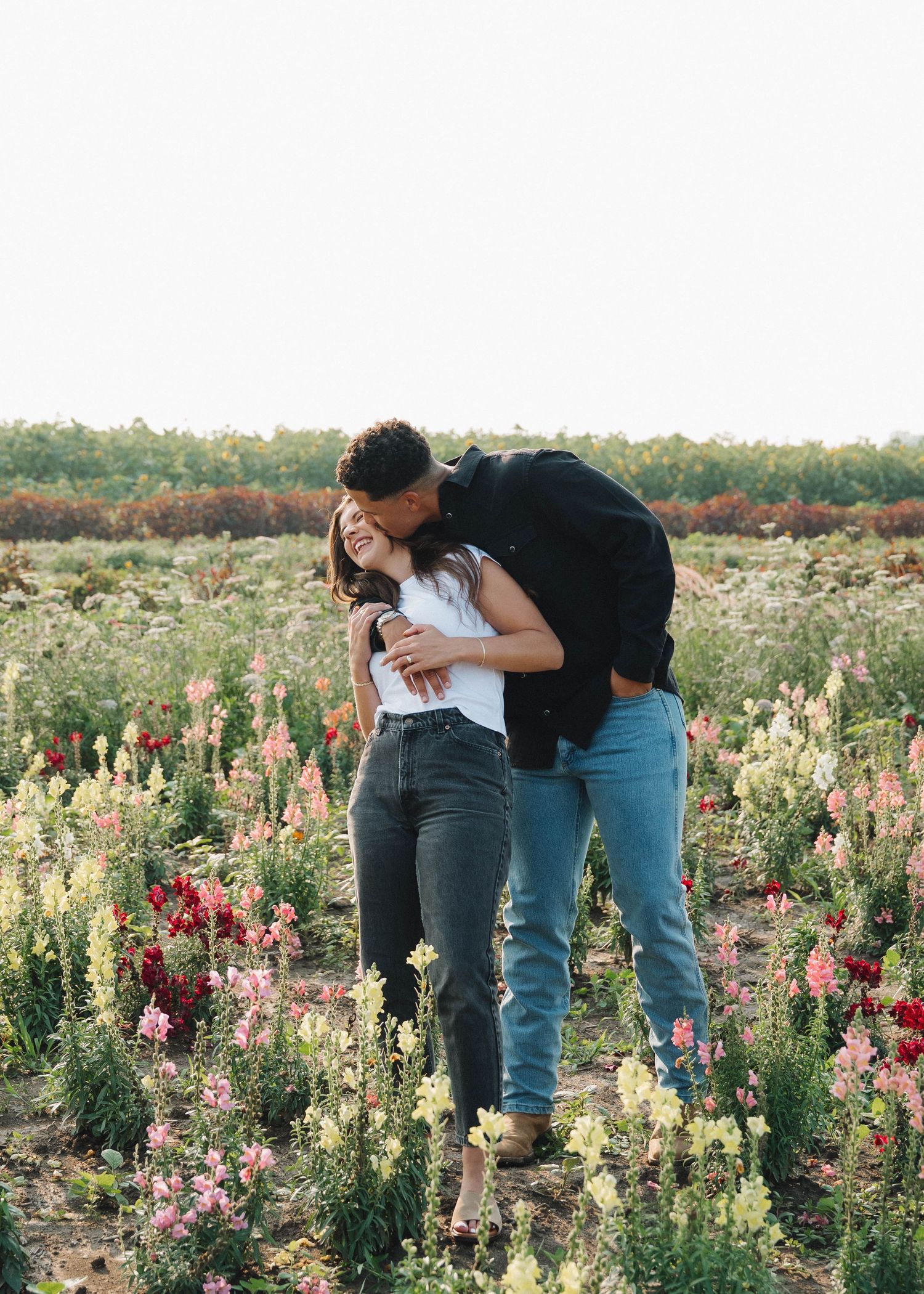 A couple shares an intimate moment while standing in a colorful wildflower field during golden hour.