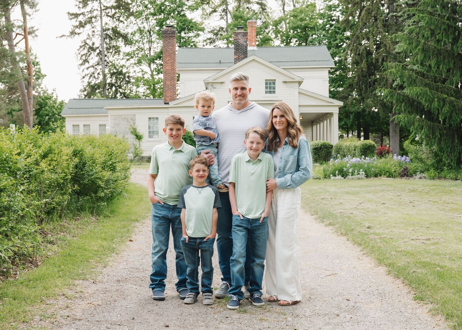 A group stands together on a gravel path surrounded by green grass and trees on a bright summer day.